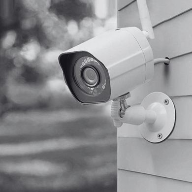 White security camera mounted on a house exterior, overlooking a yard.