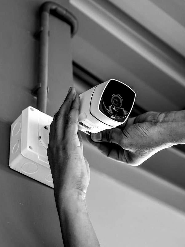 Hands mount a white security camera on a wall bracket indoors.