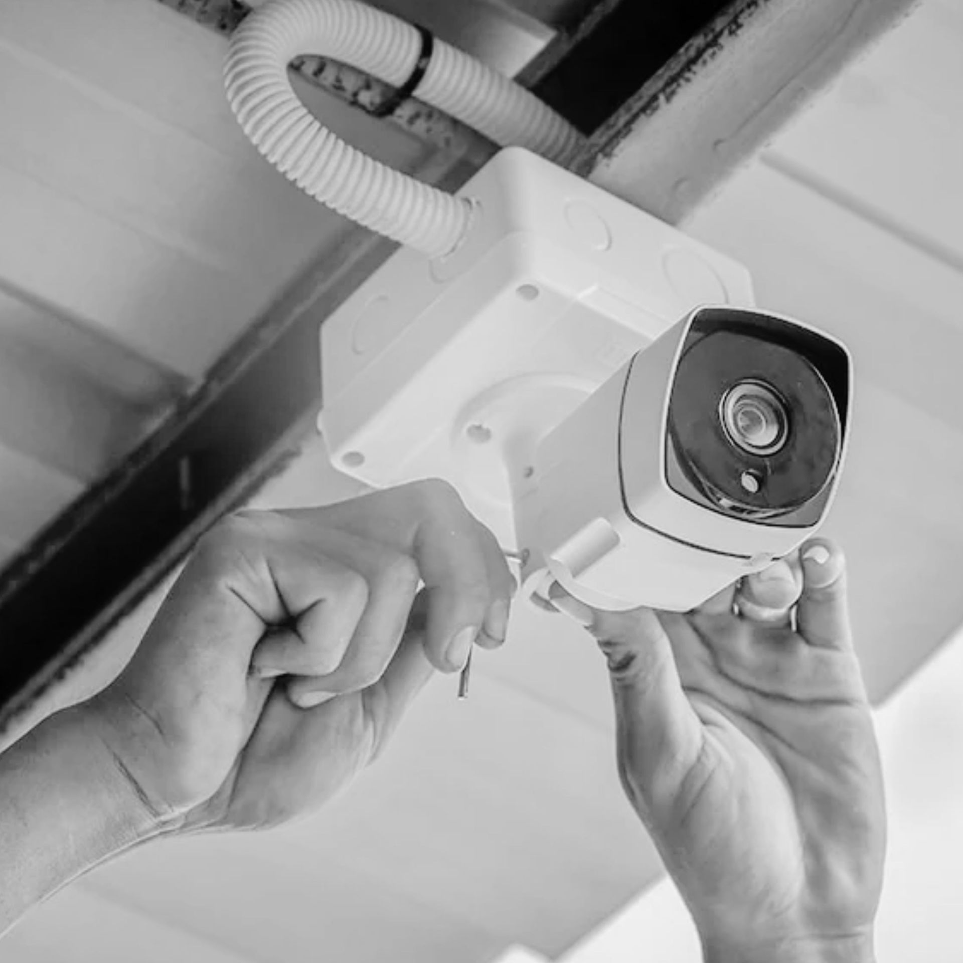 Hands adjusting a white security camera mounted on a ceiling bracket