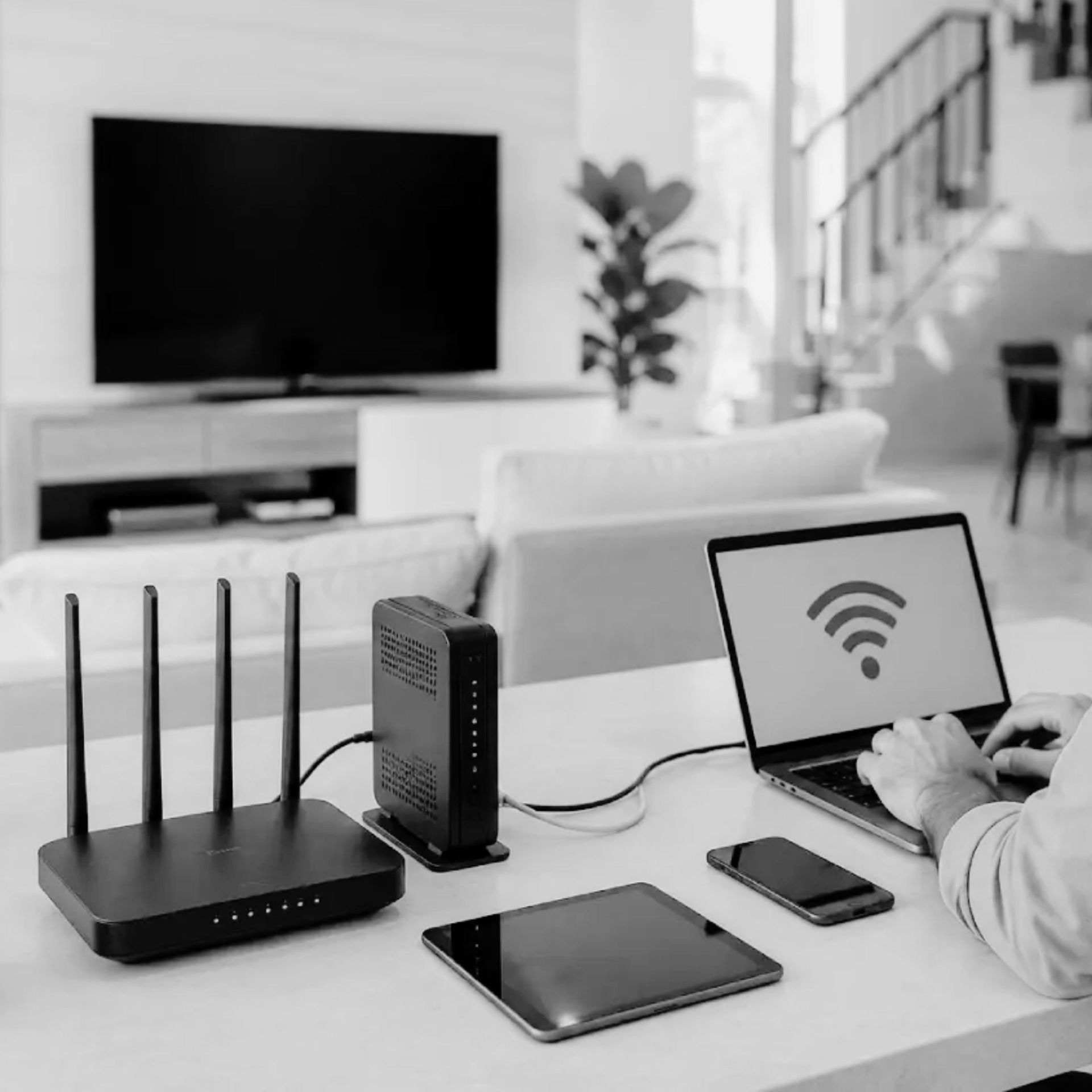 Person using laptop beside Wi‑Fi router, tablet, and phone in a living room