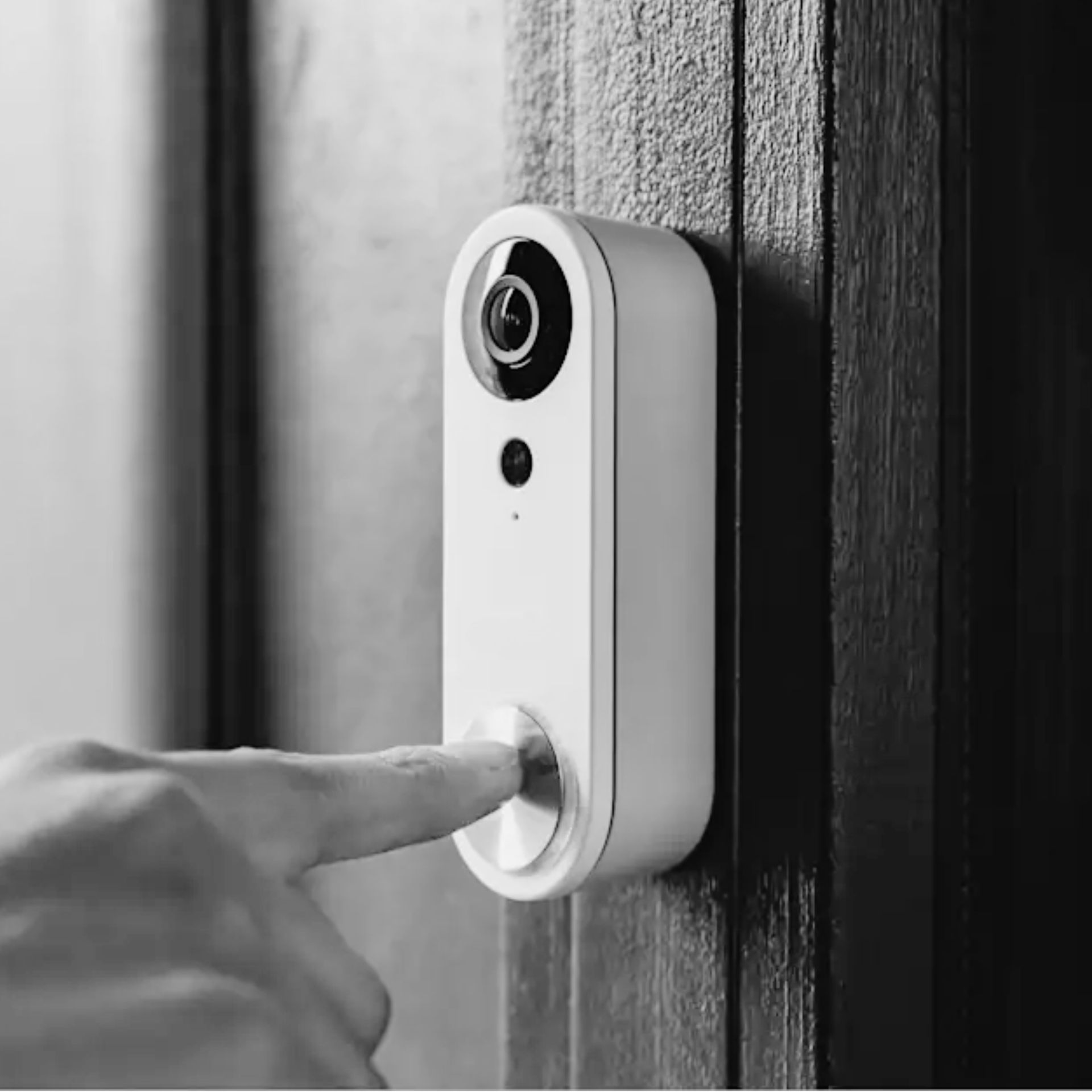 Finger pressing a white smart doorbell camera mounted on a dark wooden door.