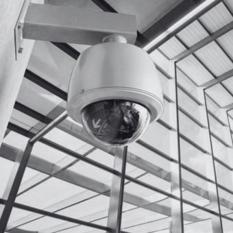 Black dome security camera mounted on a ceiling in a glass-roofed building