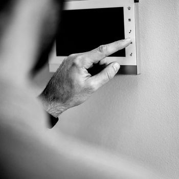 Hand pressing a wall-mounted switch panel in black and white.
