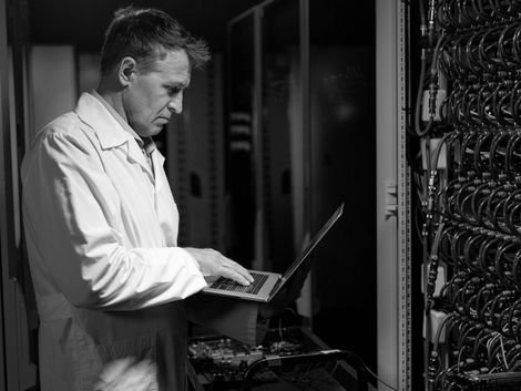 Technician in a lab coat working on a laptop beside rows of server hardware
