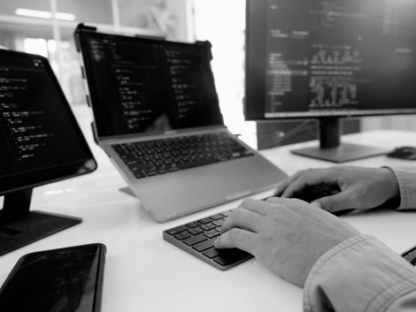 Hands typing on laptop at a desk with multiple computer monitors displaying code