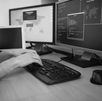 Hands typing on a keyboard beside dual monitors showing code and a world map interface