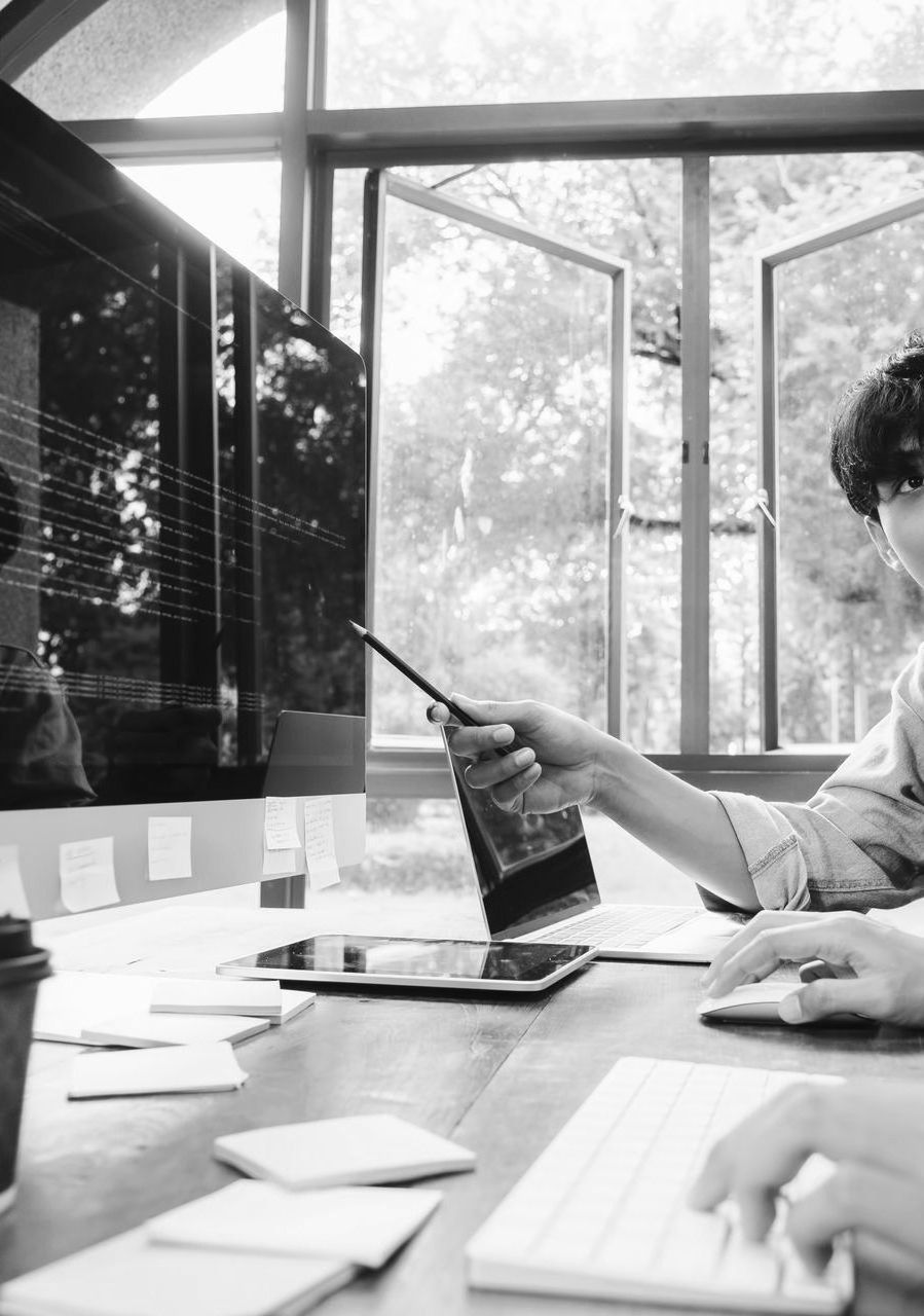 Person pointing at a laptop during a meeting in a bright office with large windows.