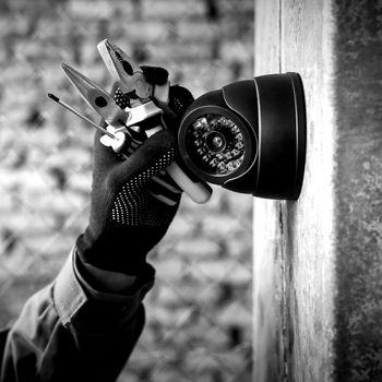 Gloved hand adjusting a wall-mounted security camera in black and white
