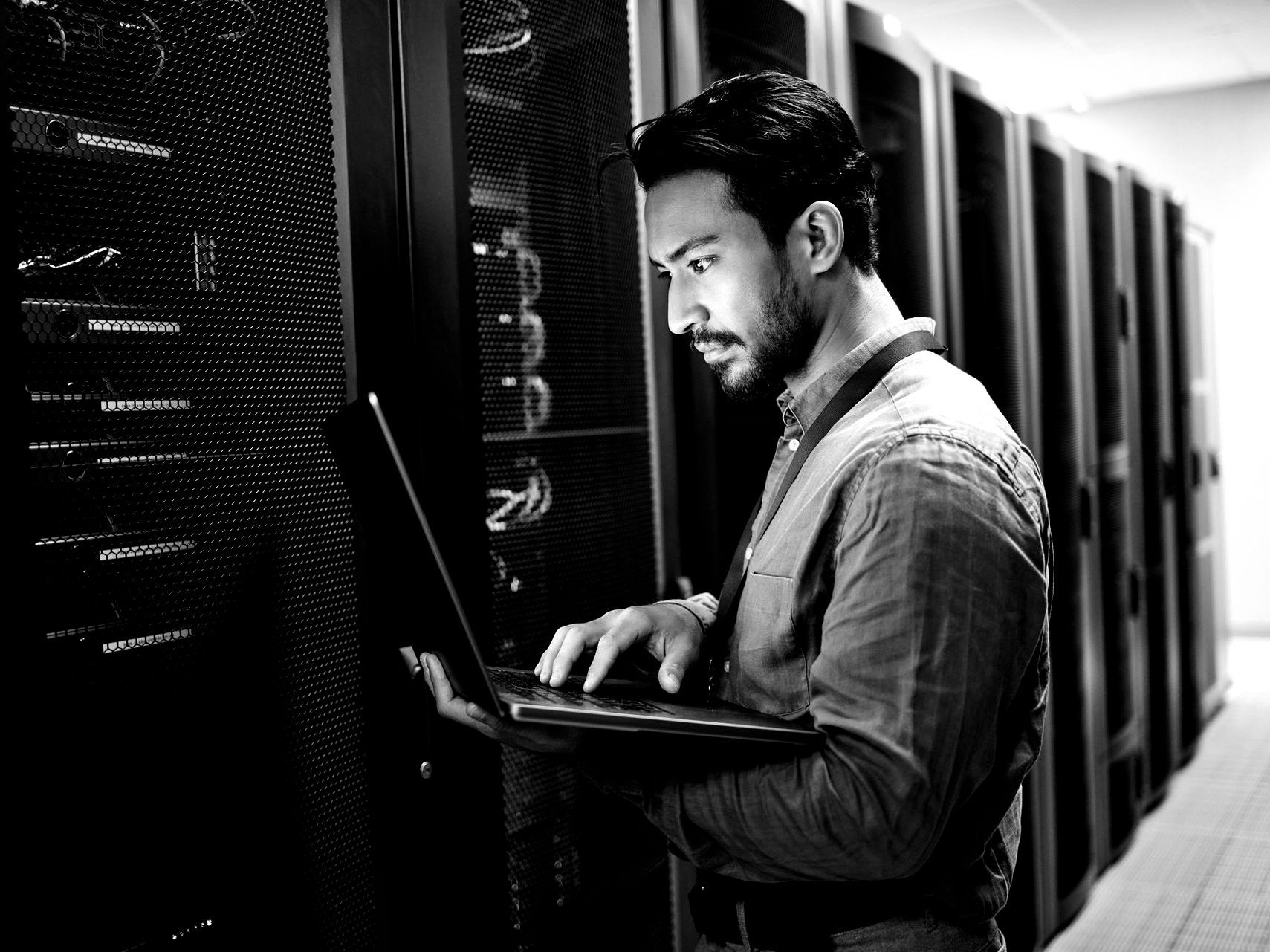Technician using a laptop in a server room beside rows of black server racks