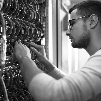 Technician adjusting wiring in a rack of cables, in black and white.