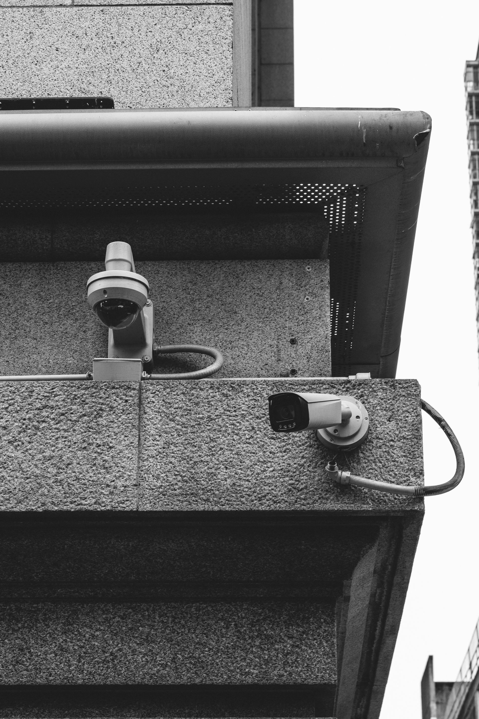 Black-and-white close-up of a building corner with mounted security cameras and wiring.