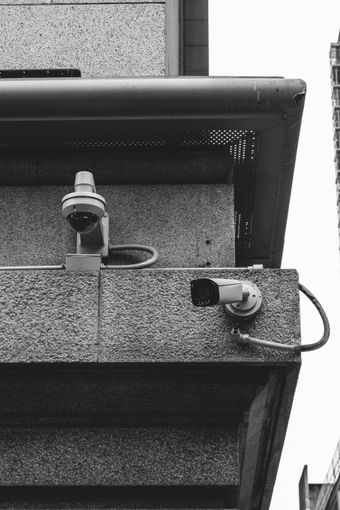 Two security cameras mounted on a building wall beneath a roof edge.