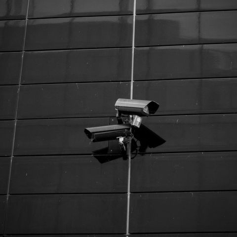Two black security cameras mounted on a dark tiled wall, centered on a vertical seam.