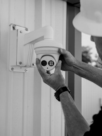 Hands installing a white security camera on a house exterior near a window