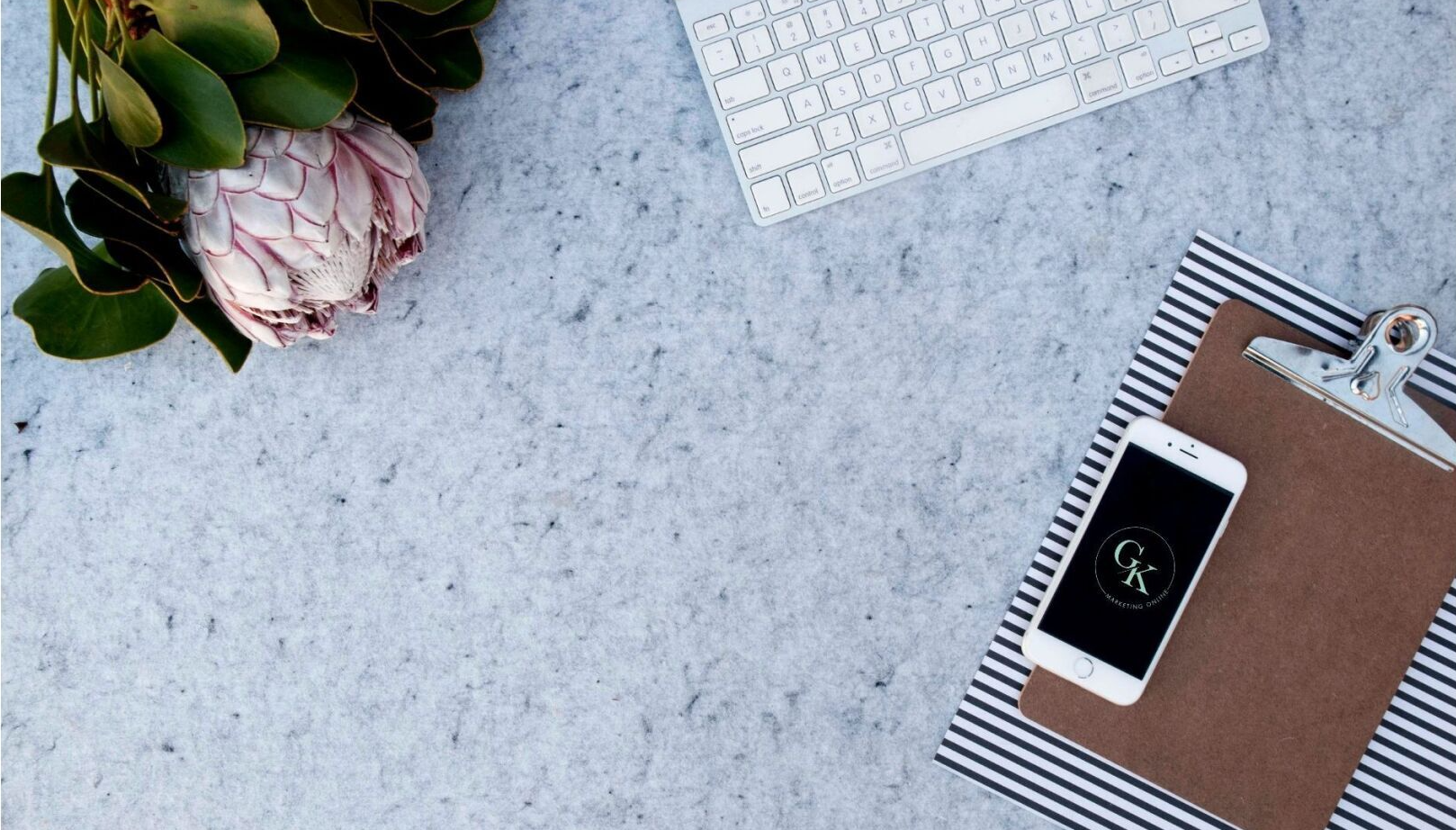 GK Marketing Online | A desk with a keyboard , cell phone , notebook and flowers.