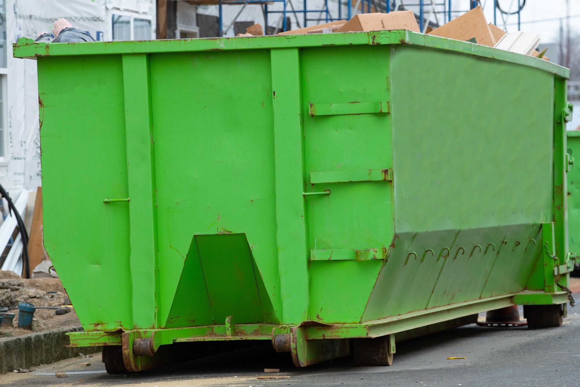 Green industrial dumpster on wheels, outdoors near a construction site. Green industrial dumpster on wheels, outdoors near a construction site.