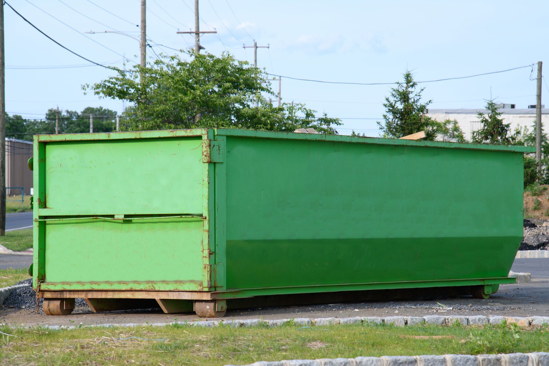 Green dumpster on a paved lot with grass, under a blue sky, by a road. Green dumpster on a paved lot with grass, under a blue sky, by a road.
