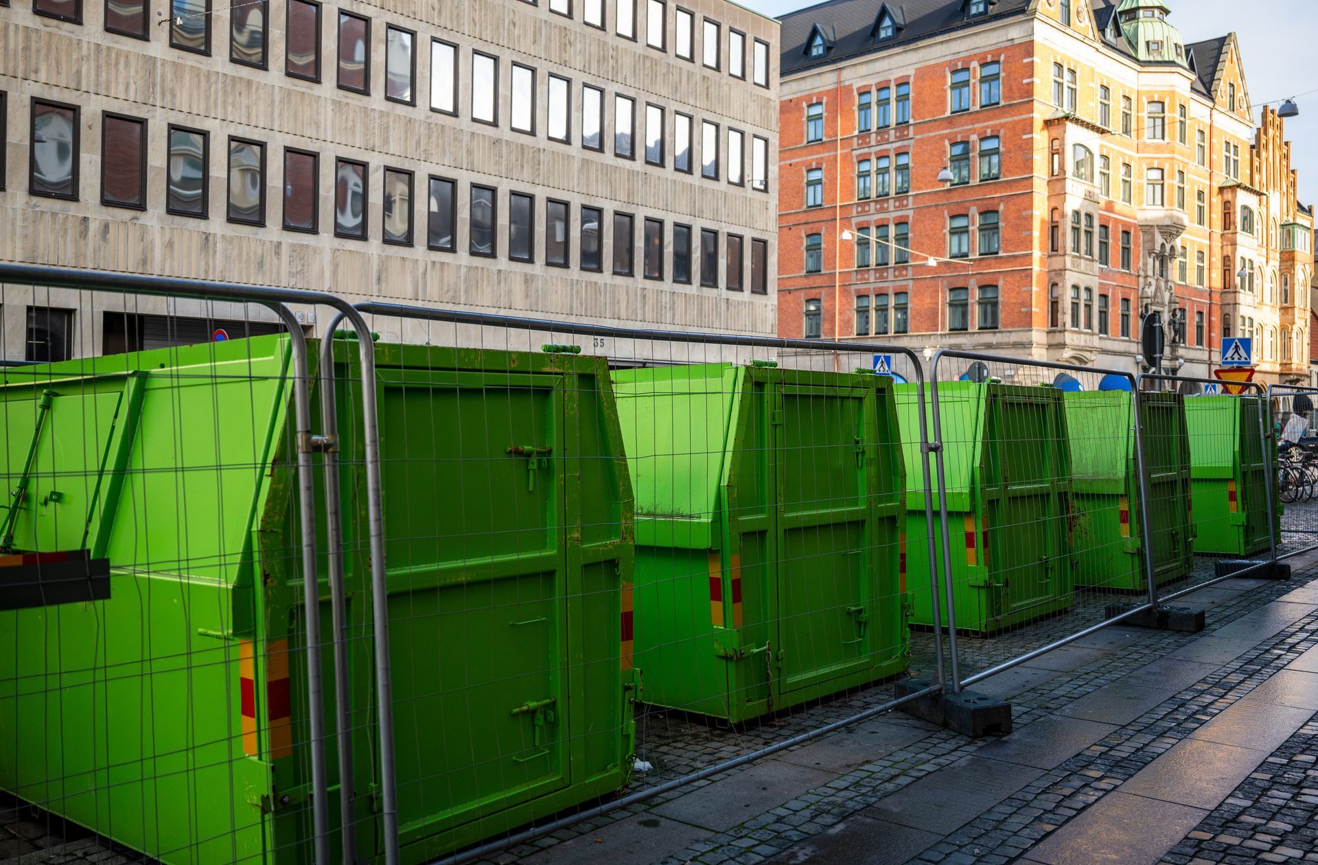 Row of green construction containers along a street with buildings. Row of green construction containers along a street with buildings.