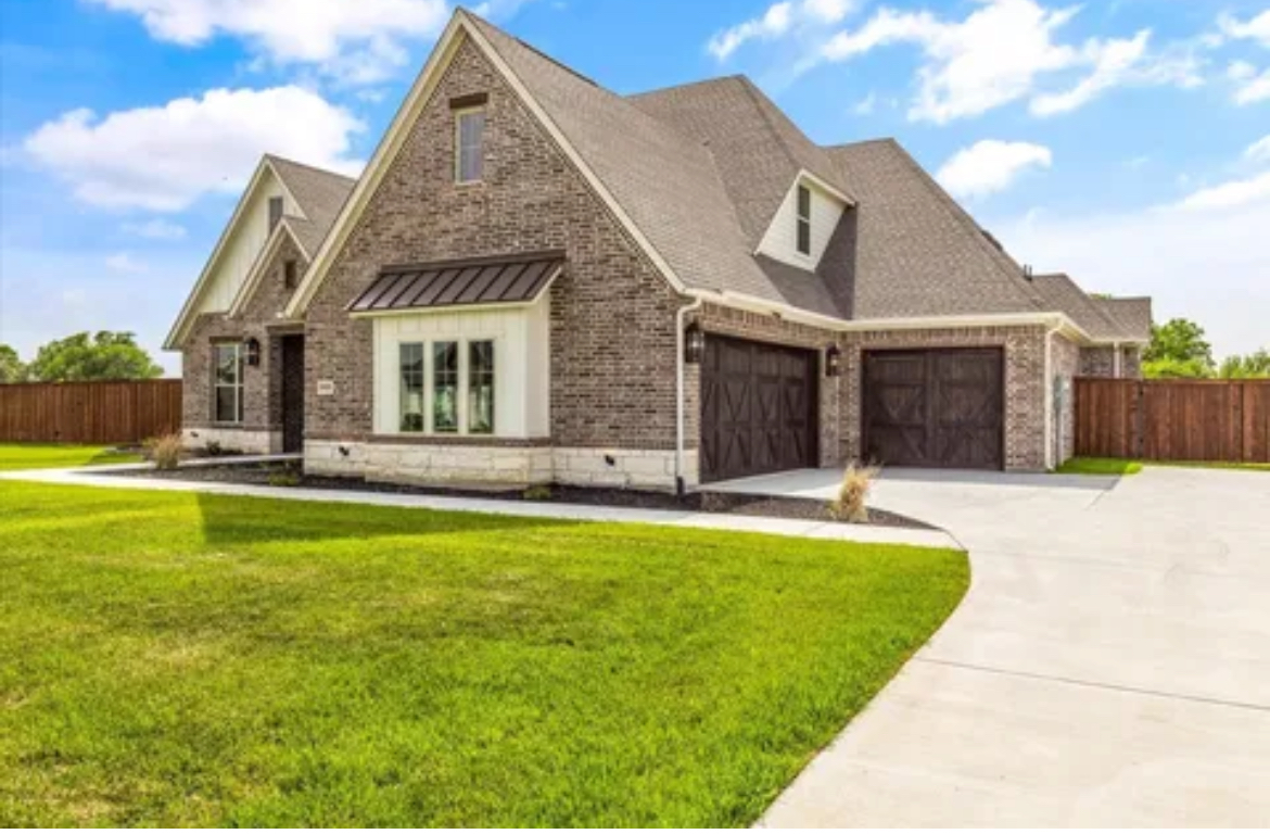 Modern stone house with steep roof, green lawn, and a wide driveway under a blue sky