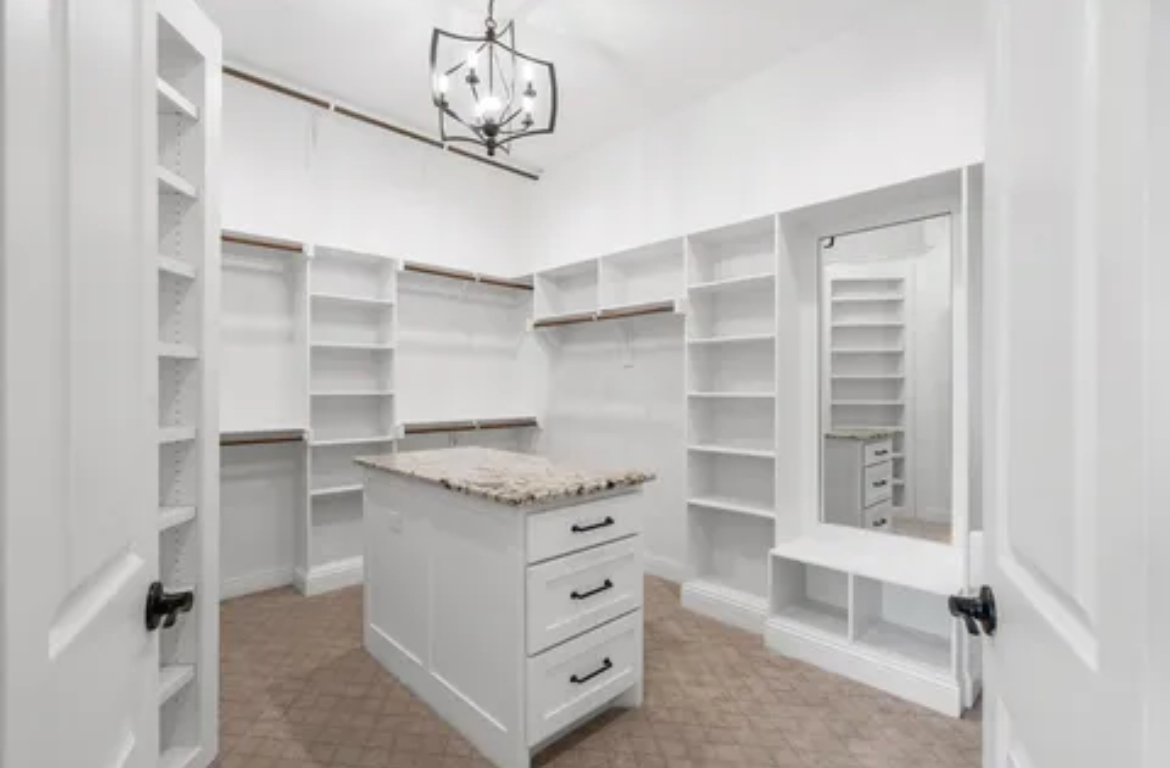 Bright walk-in closet with white built-in shelves, central island, and mirrored wall display