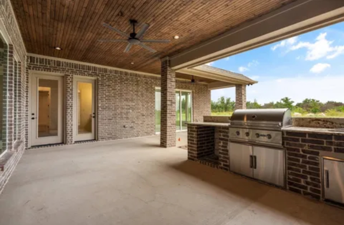 Covered backyard patio with brick walls, wood ceiling, concrete floor, and built-in stainless grill and counter.