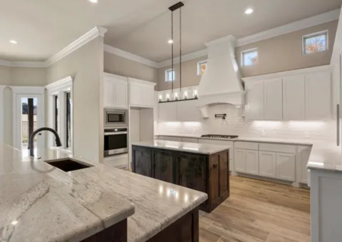 Modern white kitchen with marble island, dark wood cabinets, pendant lights, and stainless steel appliances