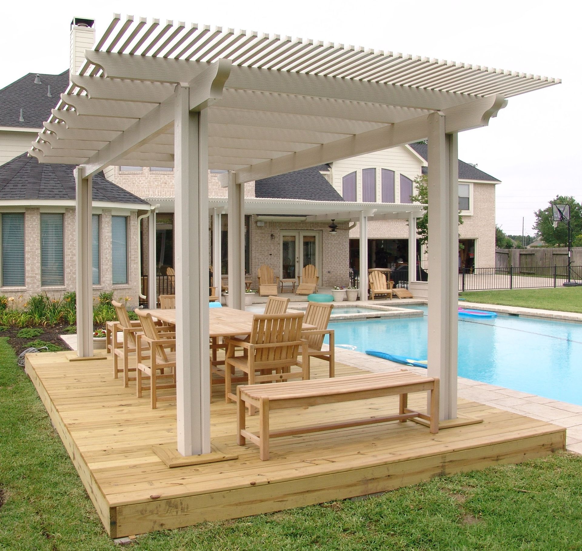 Wooden pergola-covered deck beside a swimming pool with table and chairs in a backyard