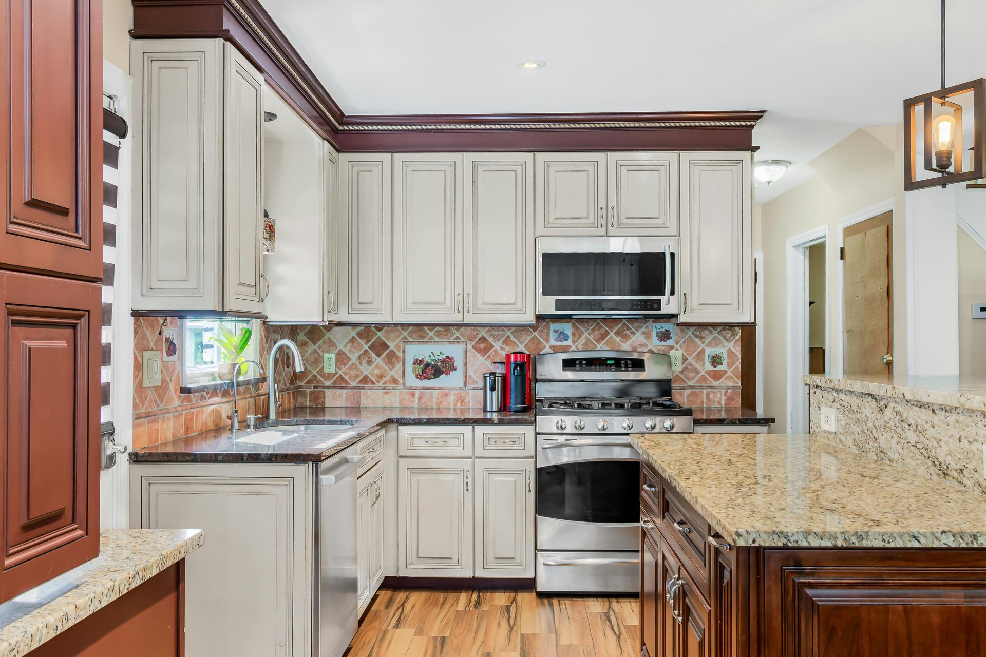 Bright modern kitchen with cream cabinets, granite counters, stainless steel appliances, and wood flooring