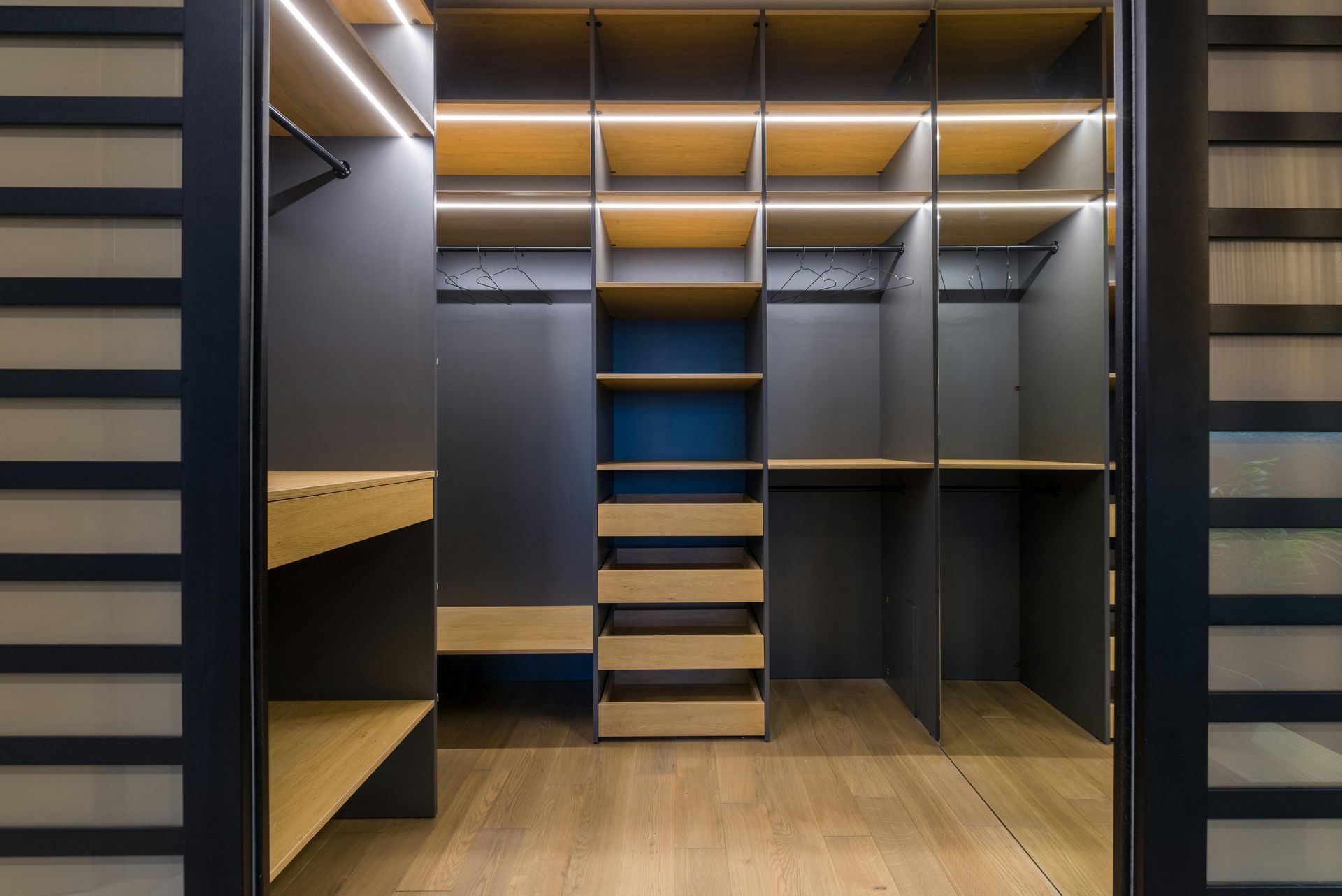 Modern walk-in closet with dark wood shelving, hanging rods, drawers, and warm lighting