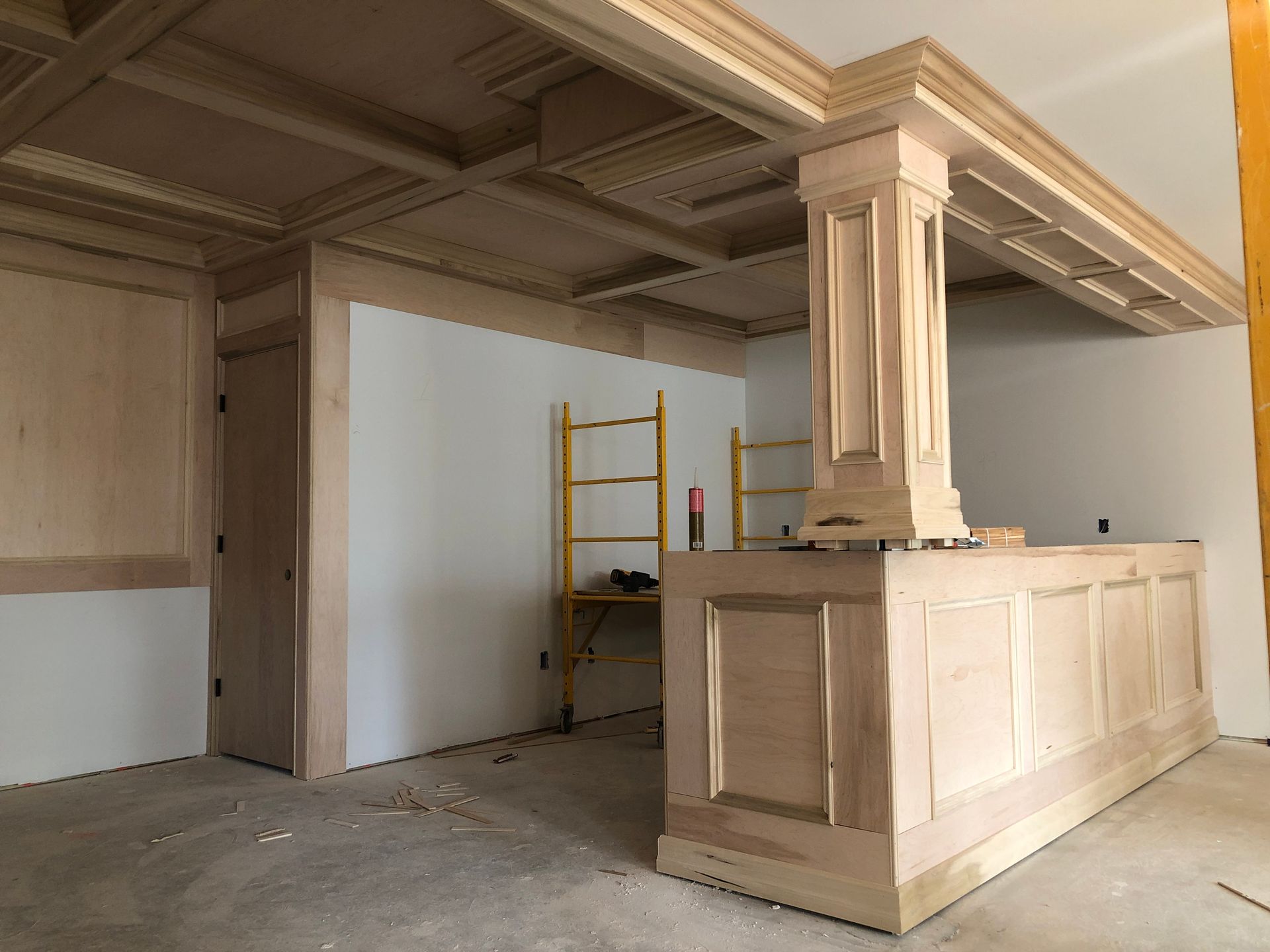 Unfinished kitchen with wooden island cabinetry, ornate ceiling details, and a yellow ladder in the background