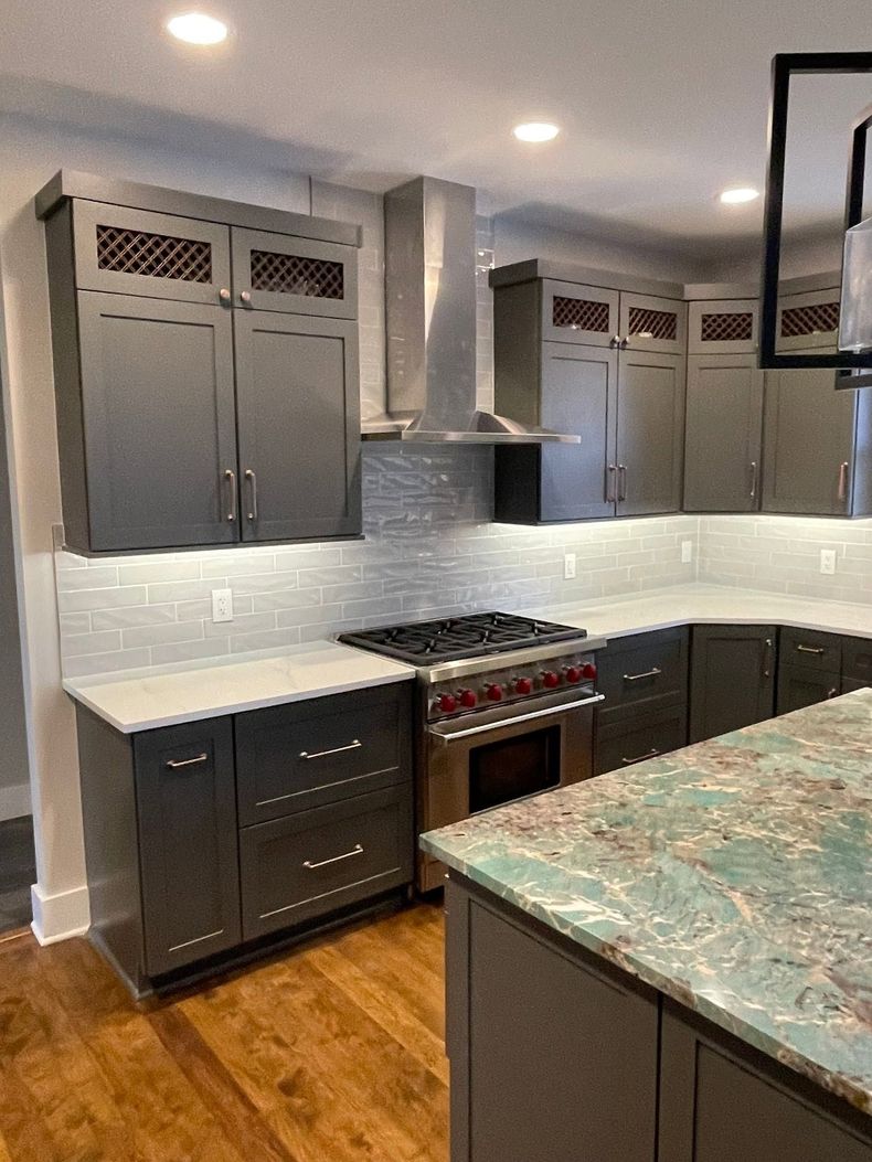 Modern kitchen with dark gray cabinets, stainless range hood, white backsplash, and wood floor
