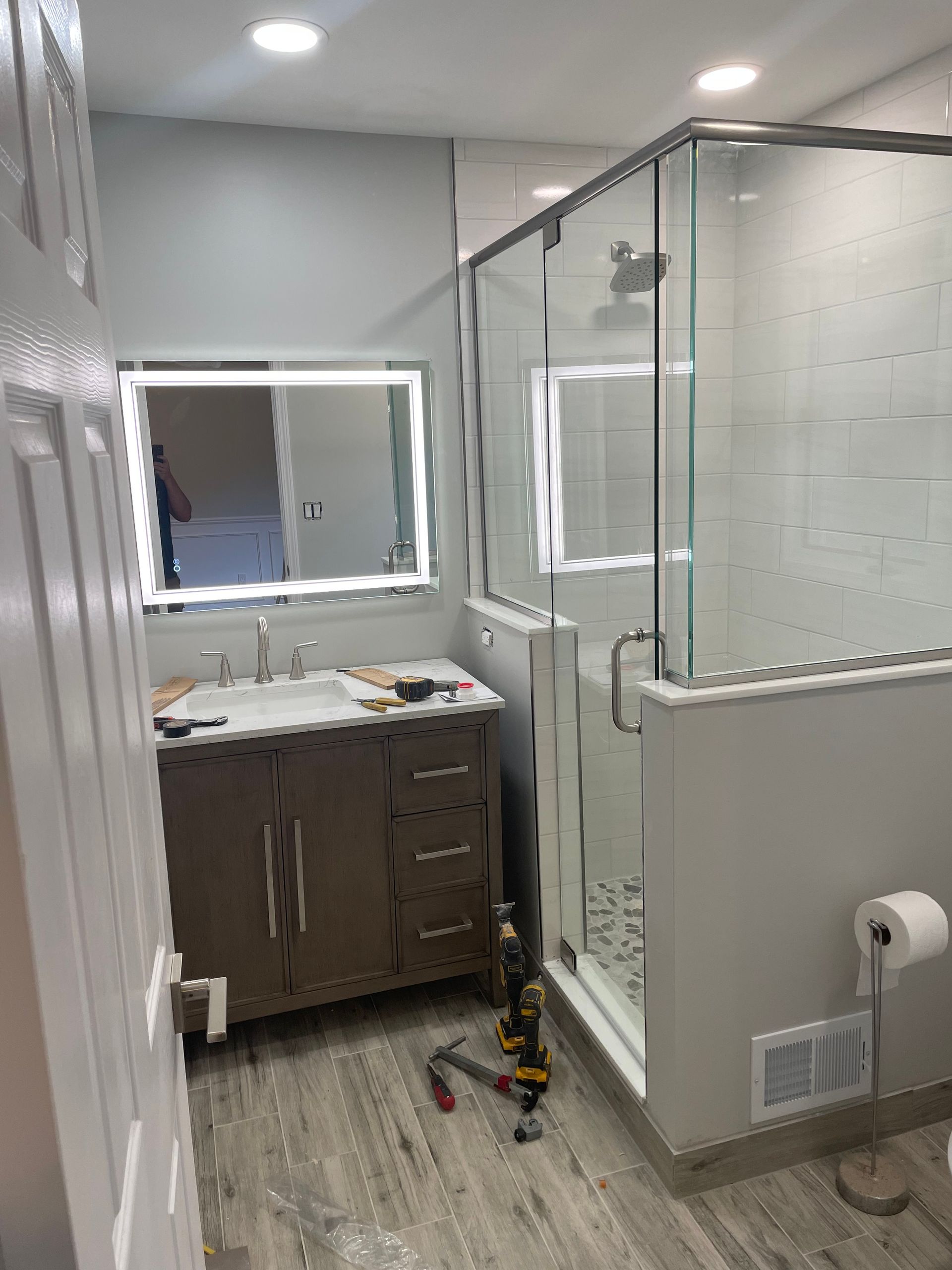 Bathroom with vanity, mirror, and glass-enclosed shower in a gray-tiled room.