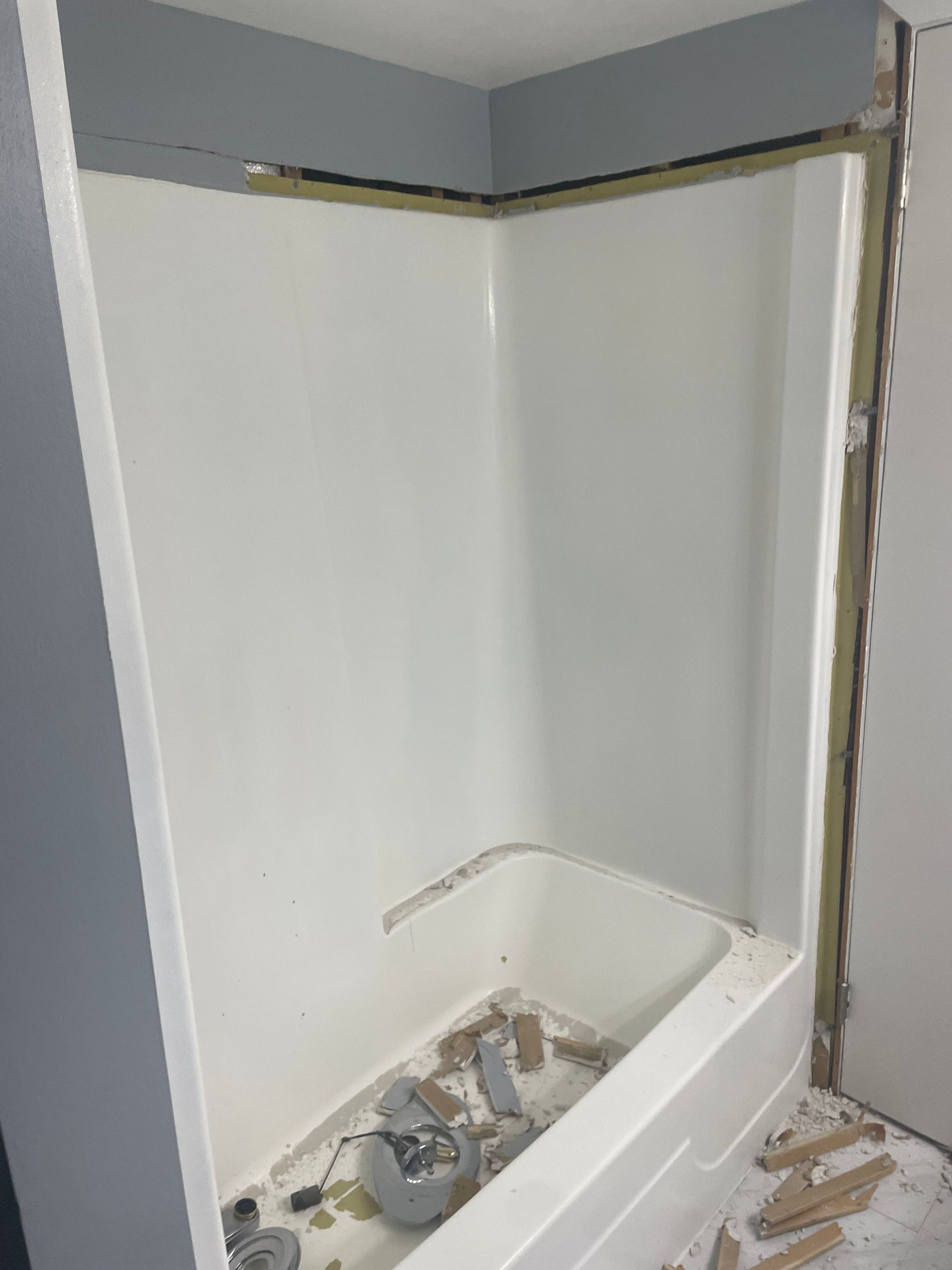 Damaged bathtub alcove with torn drywall, exposed framing, and construction debris on the floor