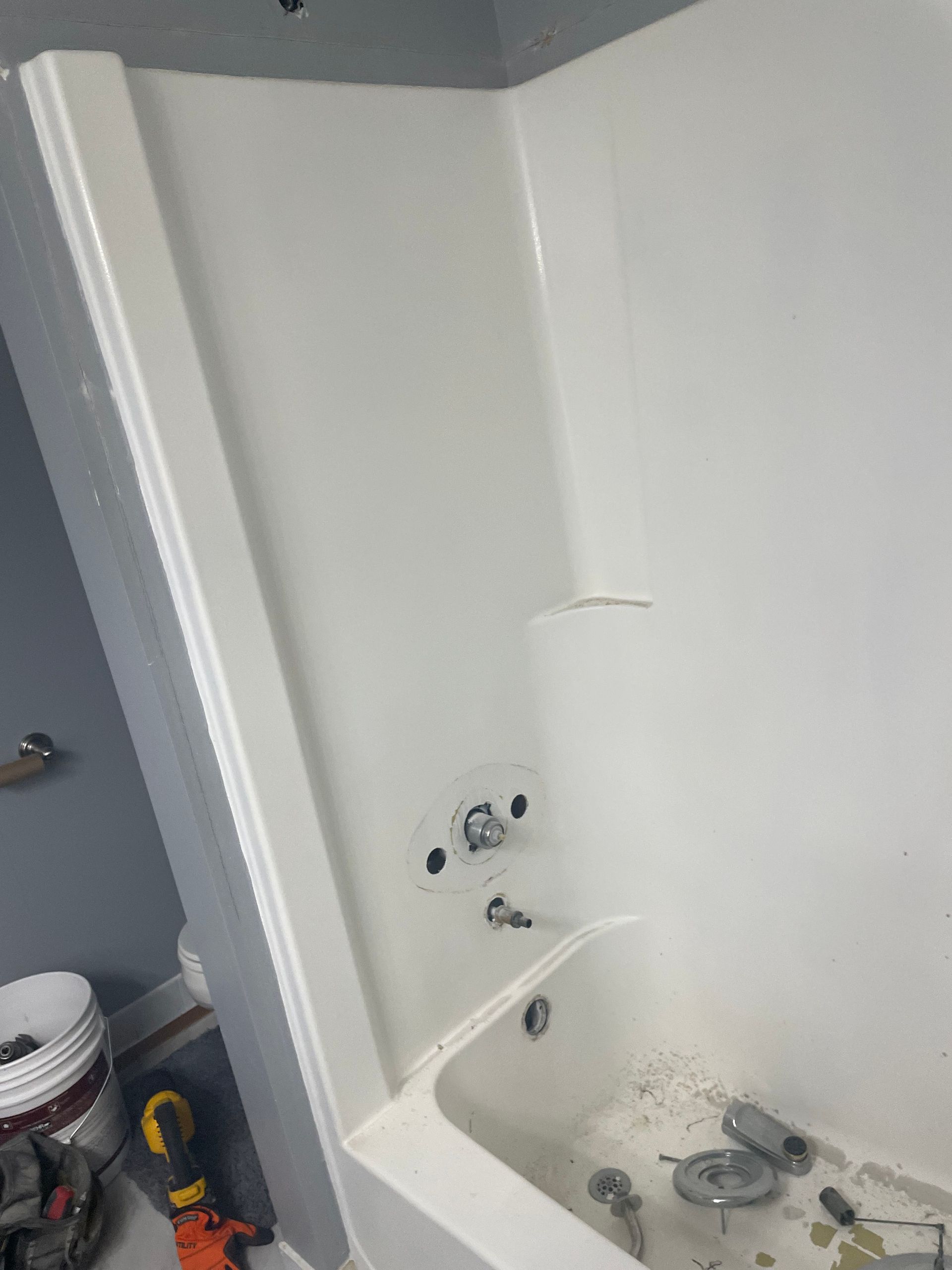 Small white bathroom with a bathtub, shower fixtures, and a paint bucket and tools on the floor.