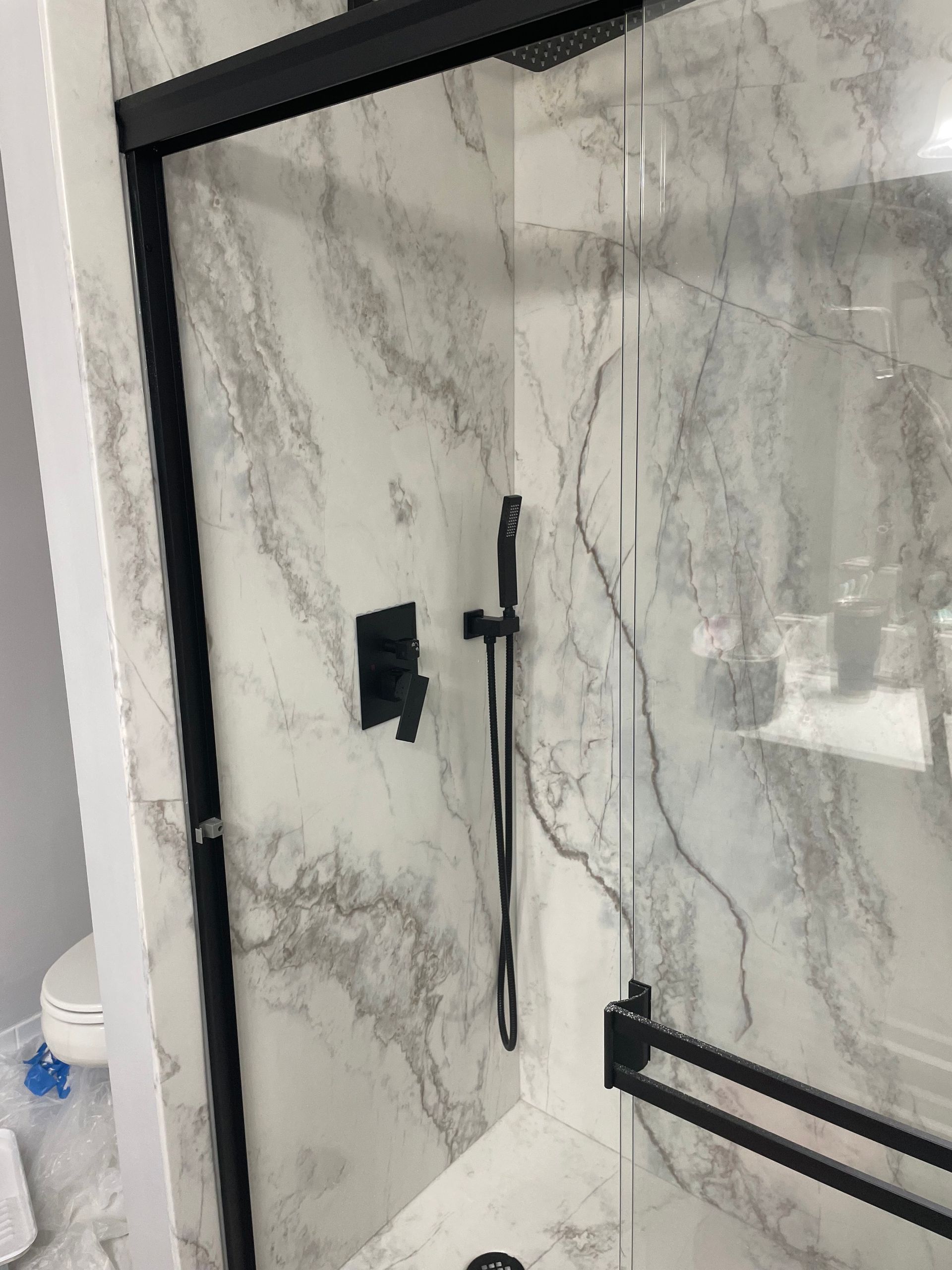 Marble-tiled shower with black glass door frame and wall-mounted shower controls
