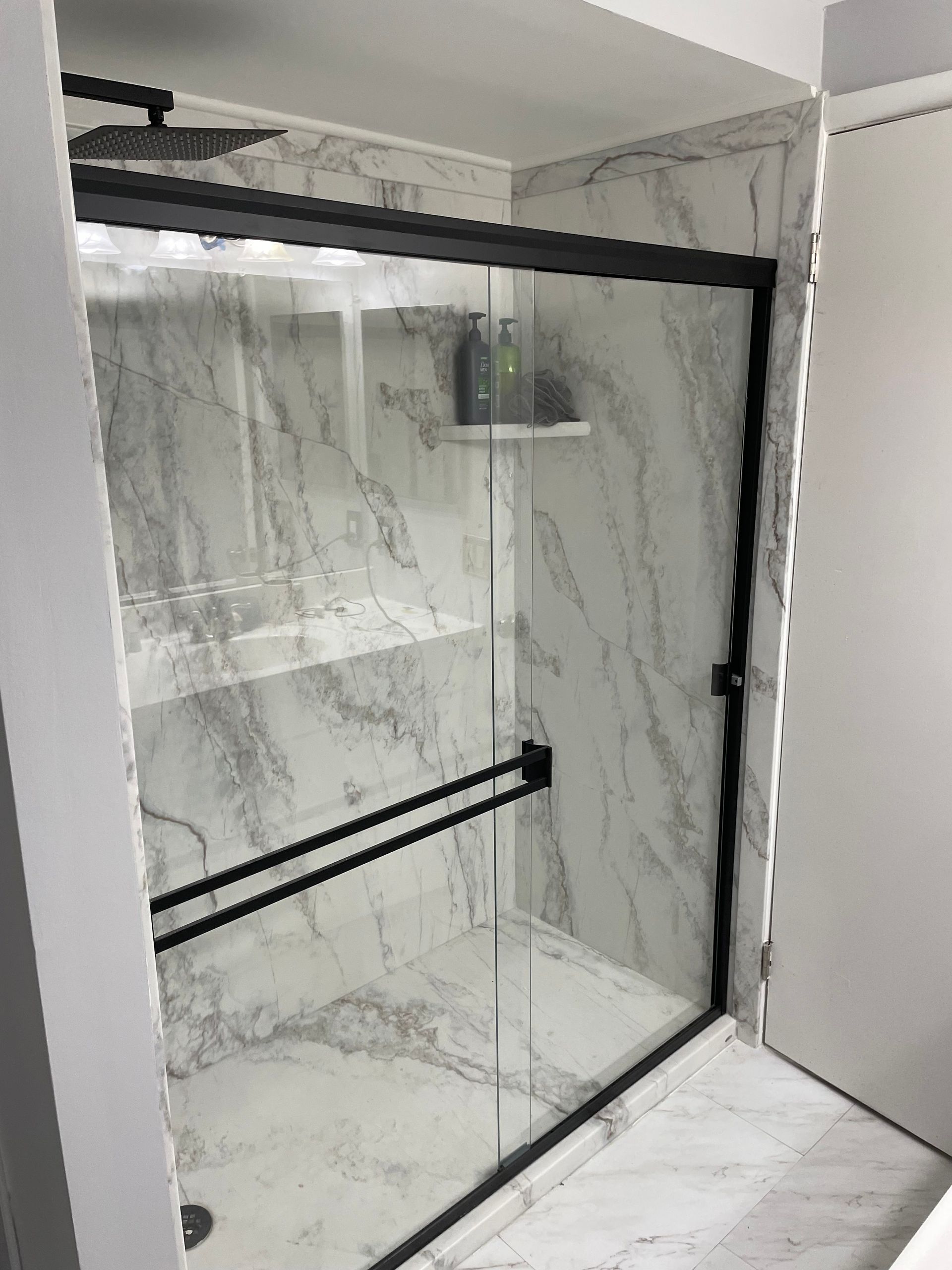 Glass shower enclosure with black frame in a marble-tiled bathroom