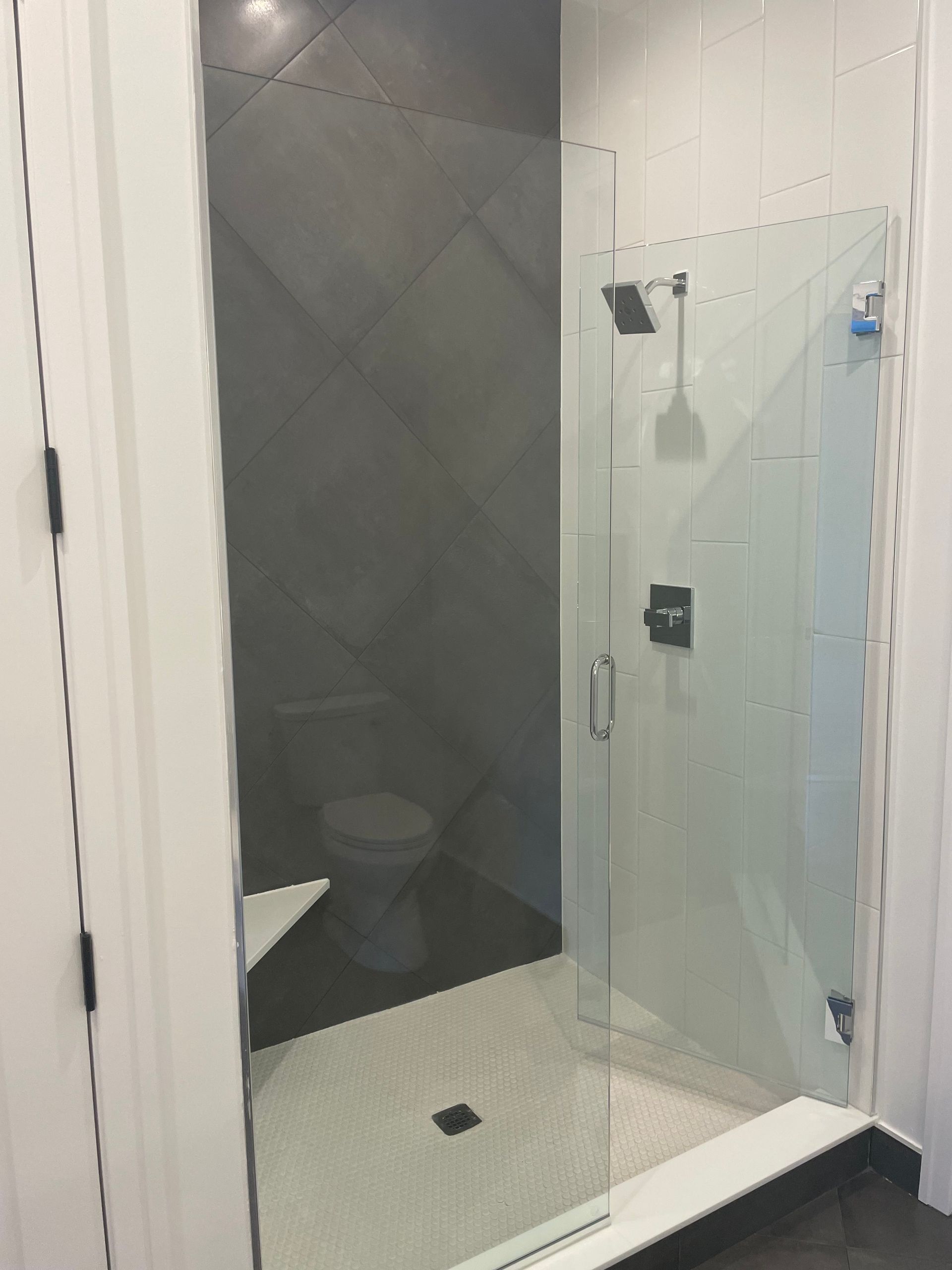 Modern bathroom shower with clear glass door, tiled walls, and visible toilet behind frosted panel