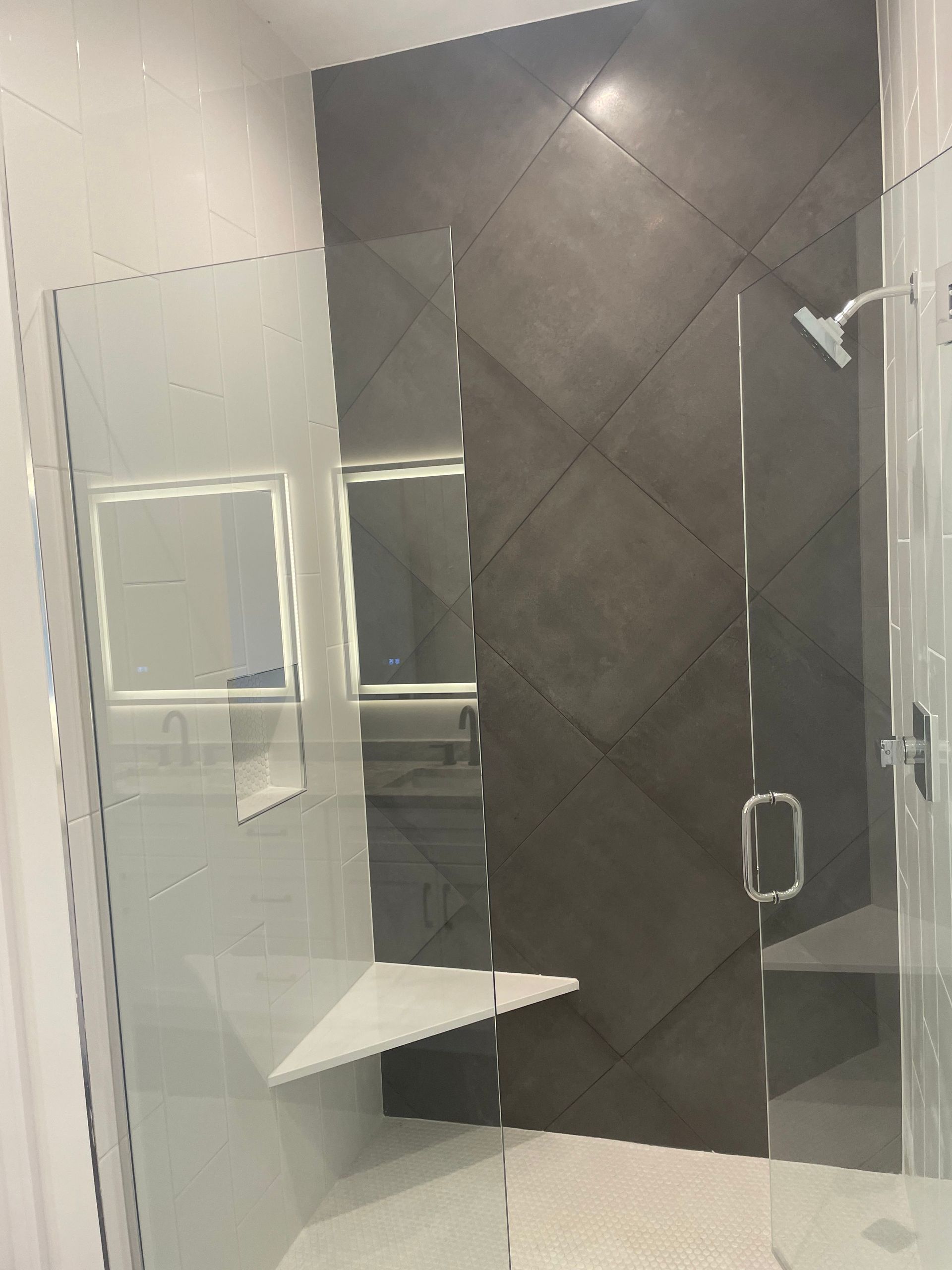 Small bathroom with glass shower doors, dark gray tiled shower wall, and a white corner shelf.