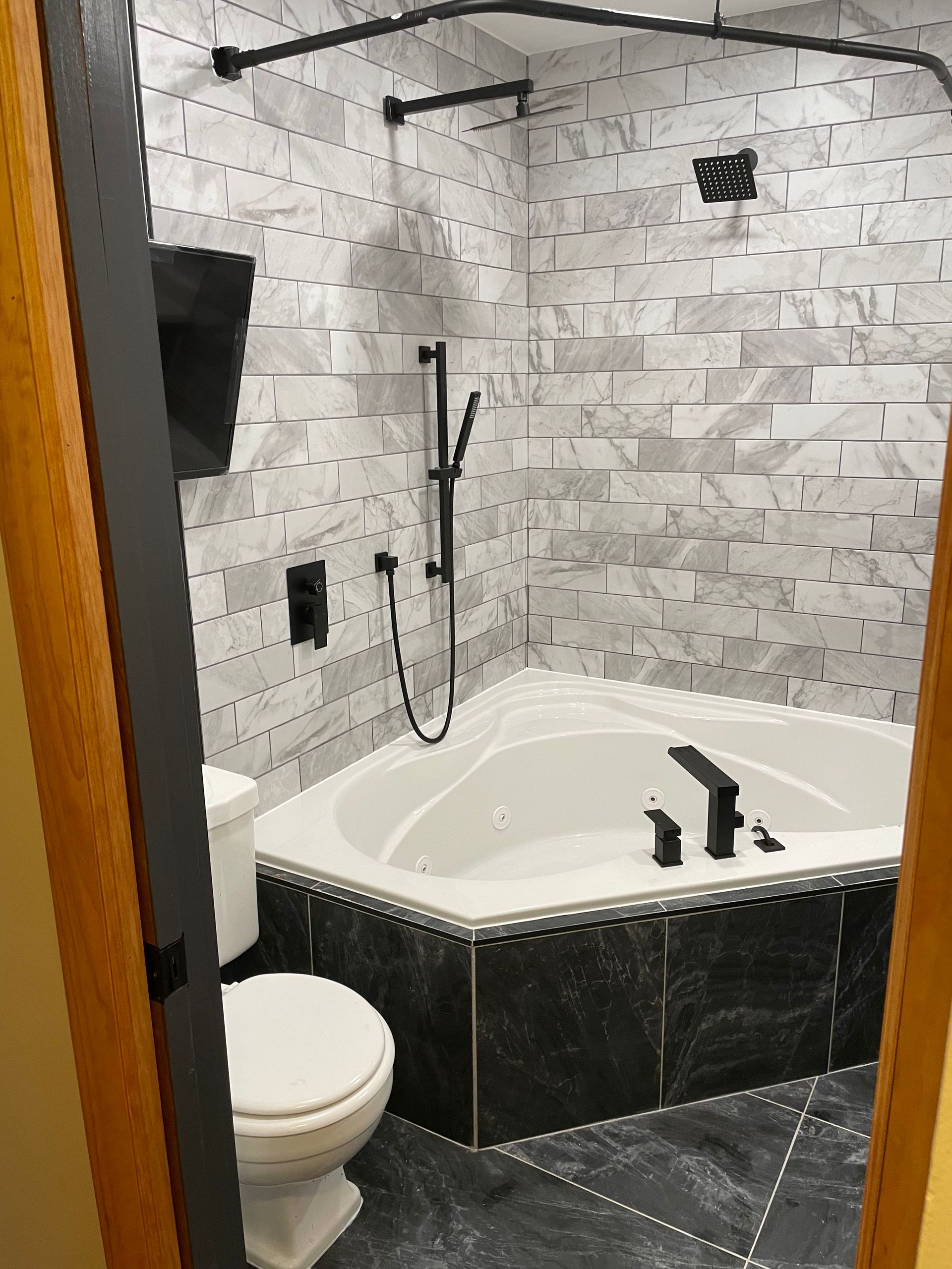 Modern bathroom with corner jetted tub, handheld shower, toilet, and gray stone tile walls and floor