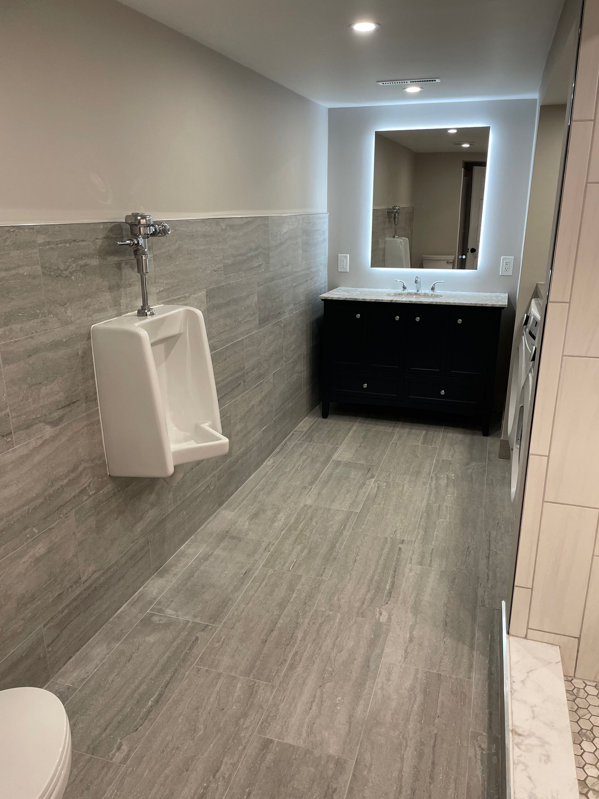 Accessible restroom with urinal, sink, black vanity, and large mirror on gray walls and floor