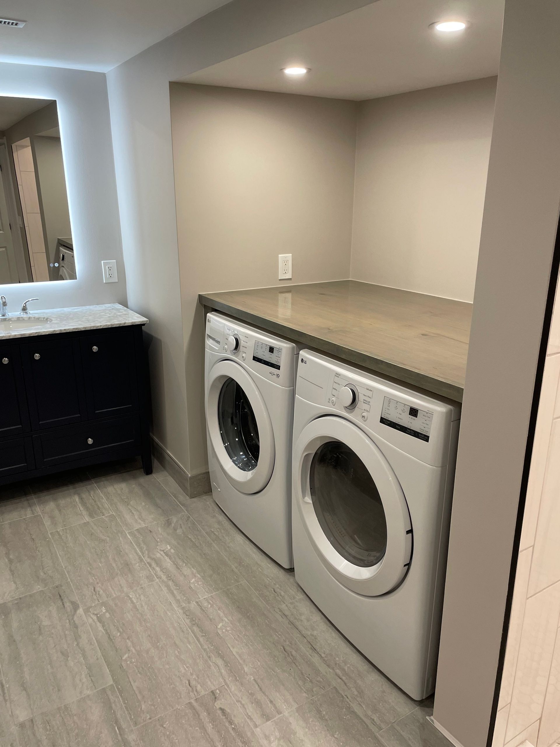 Laundry room with two front-loading washer-dryers under a countertop and a sink on the left.