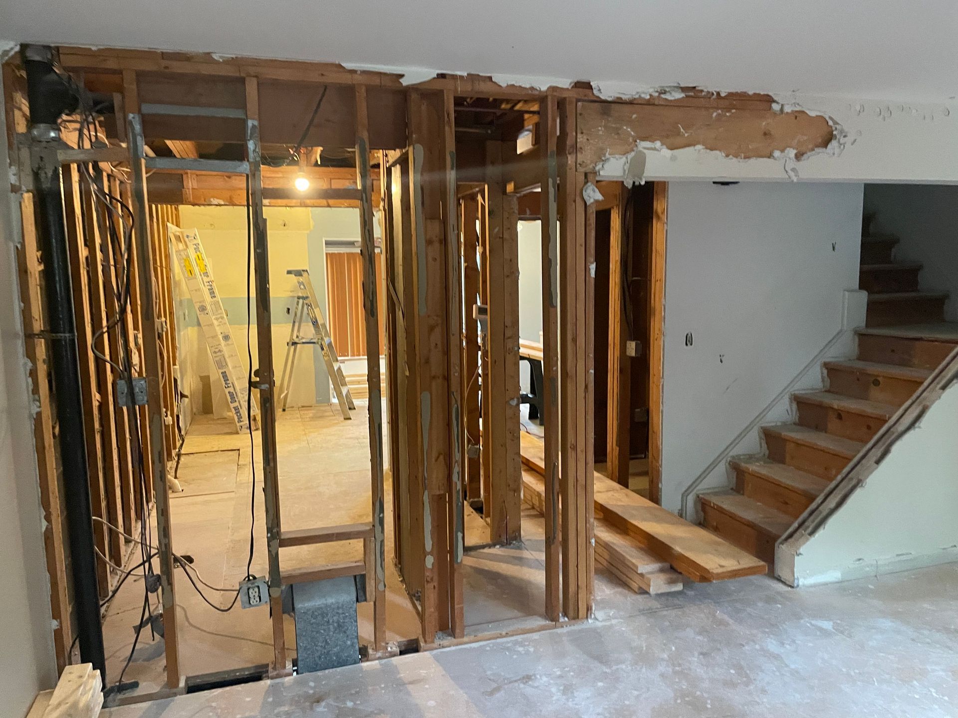 Interior under renovation with exposed studs, wiring, and a staircase on the right