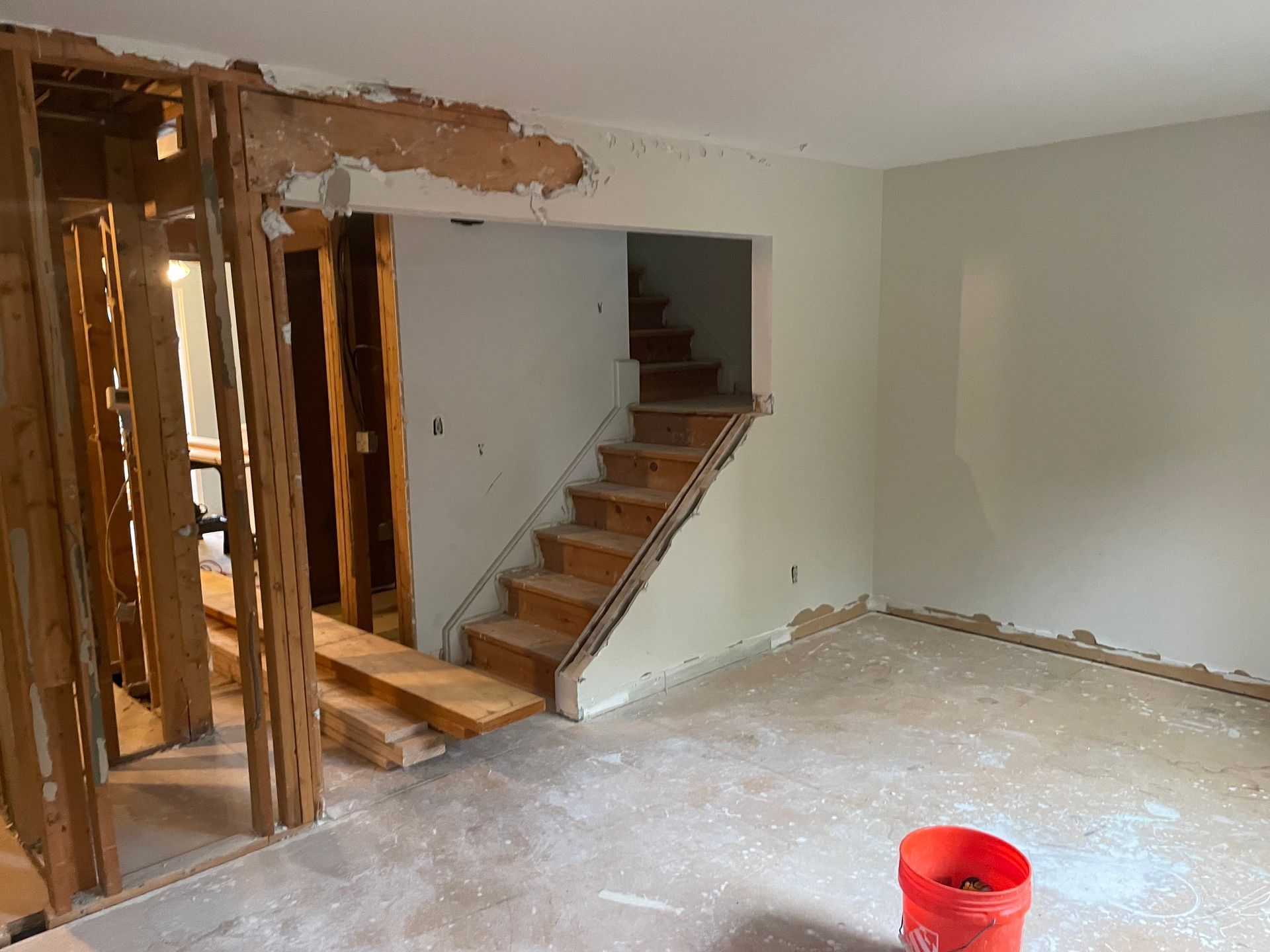Partially demolished room with exposed framing, staircase, and a red bucket on the floor