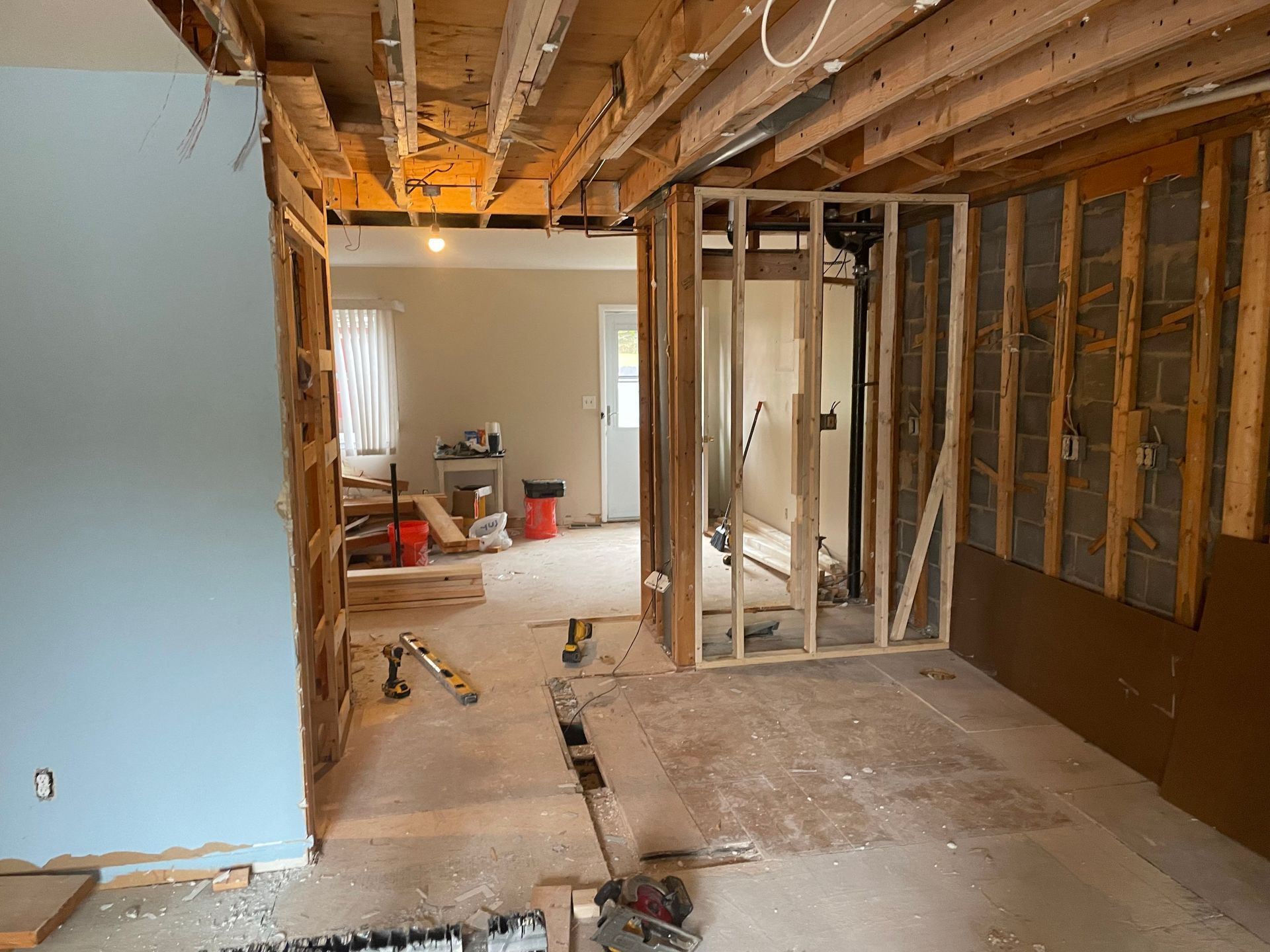 Interior under renovation with exposed studs, open ceiling joists, and construction tools on the floor.