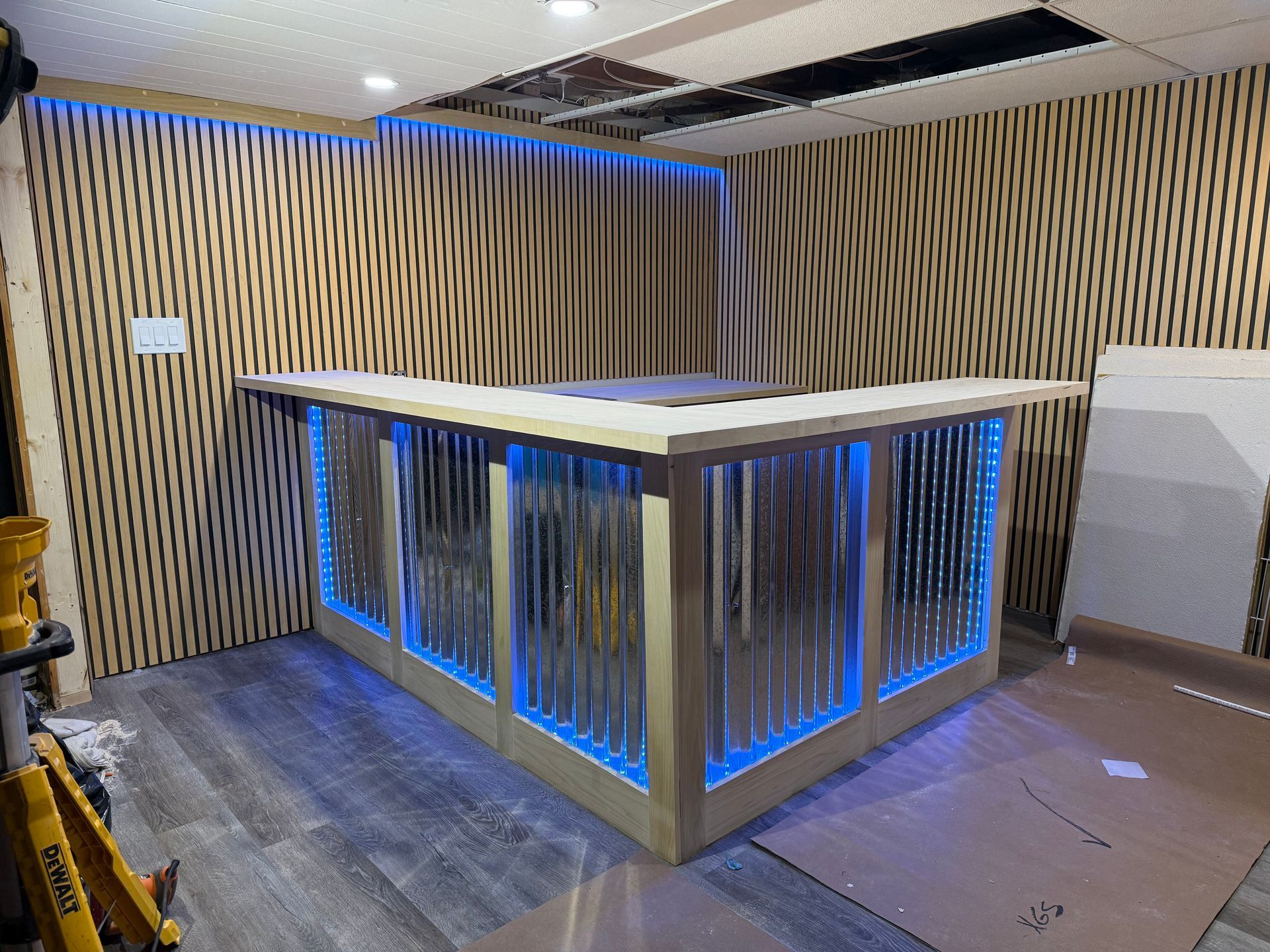 Interior with a wooden bar counter, blue LED lighting, and patterned wood wall panels under construction