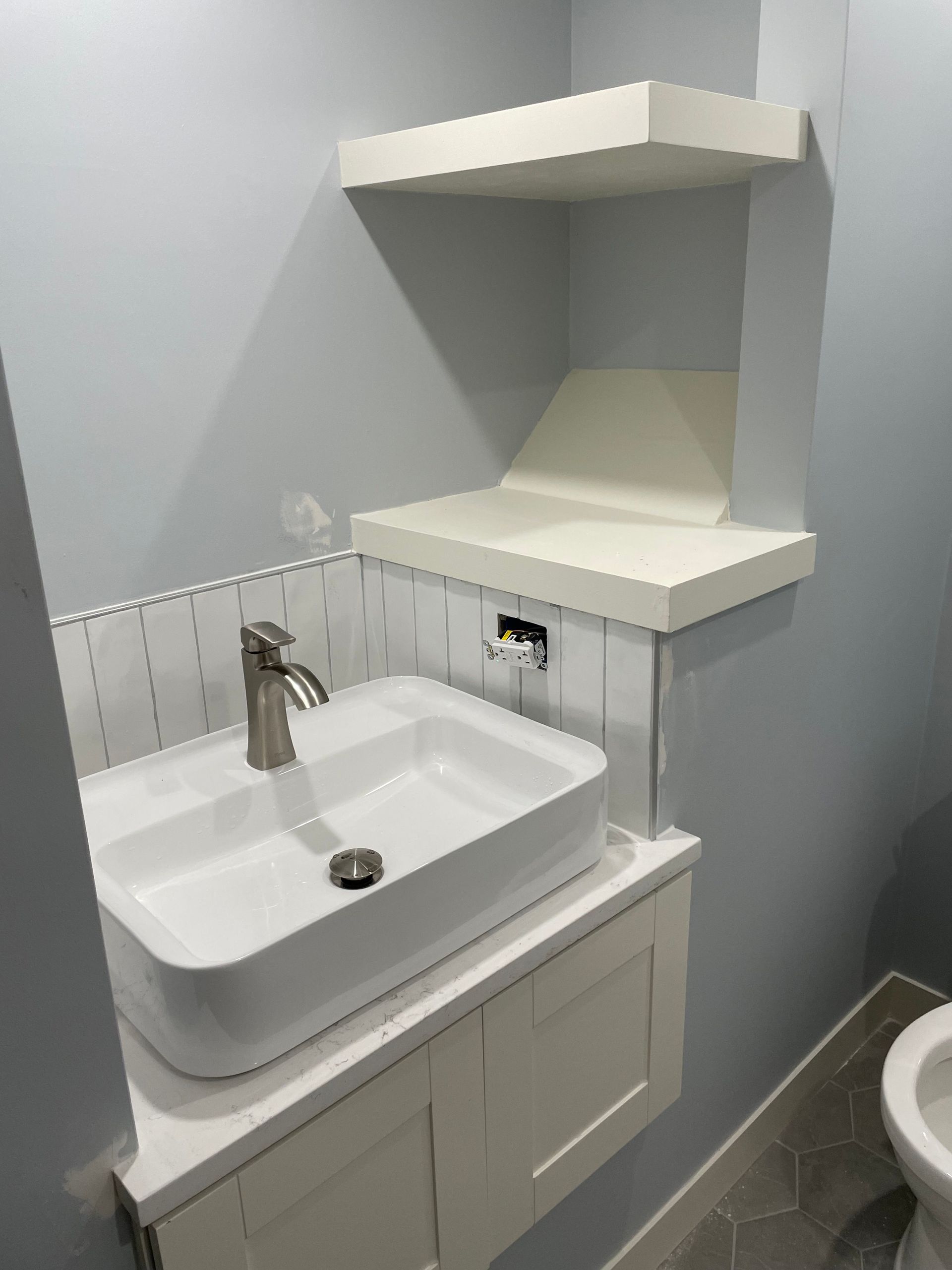 Small bathroom vanity with white sink, mirror shelf, and toilet visible to the right.