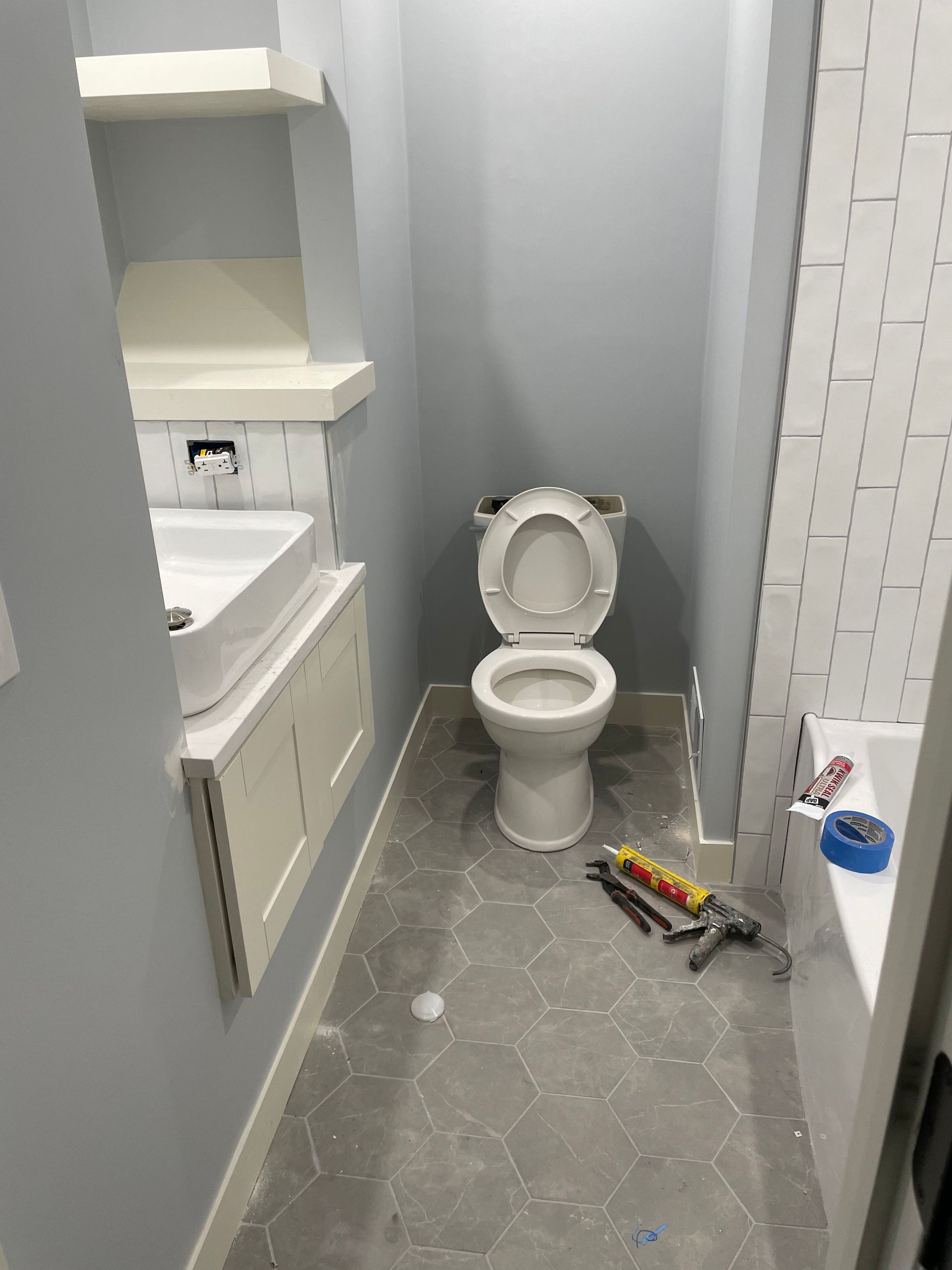 Small bathroom under renovation with a toilet, vanity, tile floor, and tools on the floor.