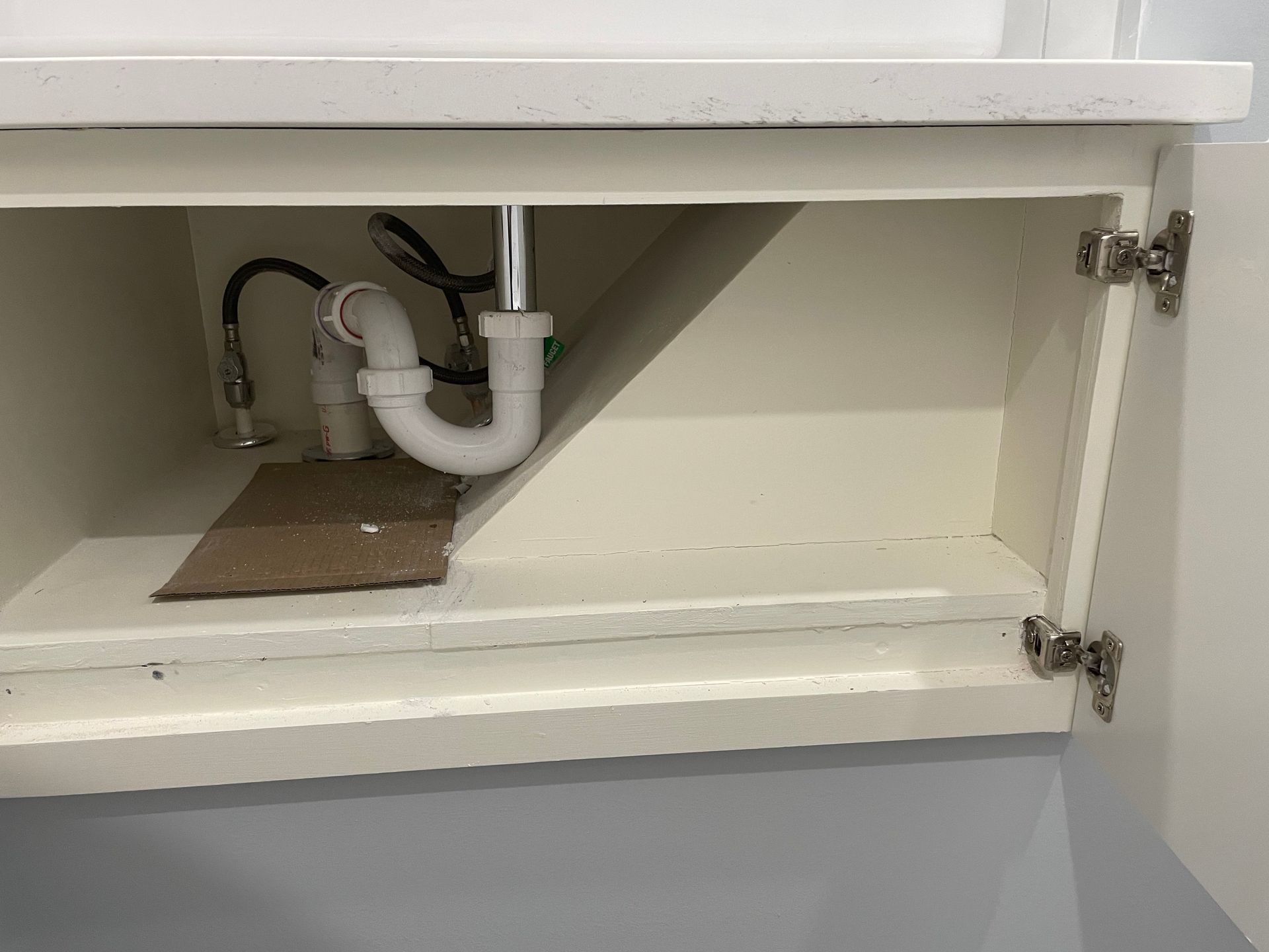 Open cabinet under sink with visible white plumbing pipes and a drain trap.