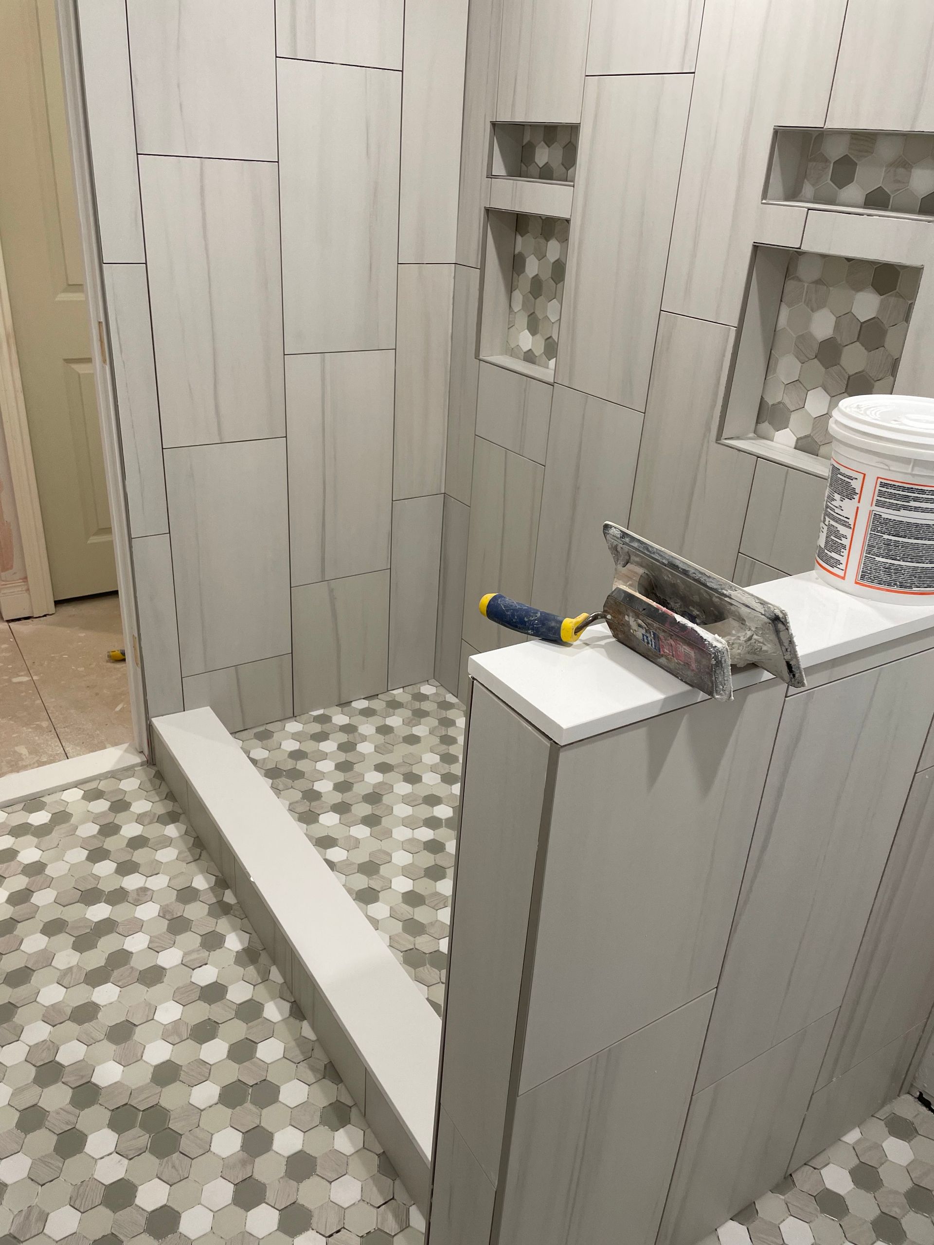 Small tiled bathroom with a walk-in shower, vanity counter, and cleaning tools on a shelf.