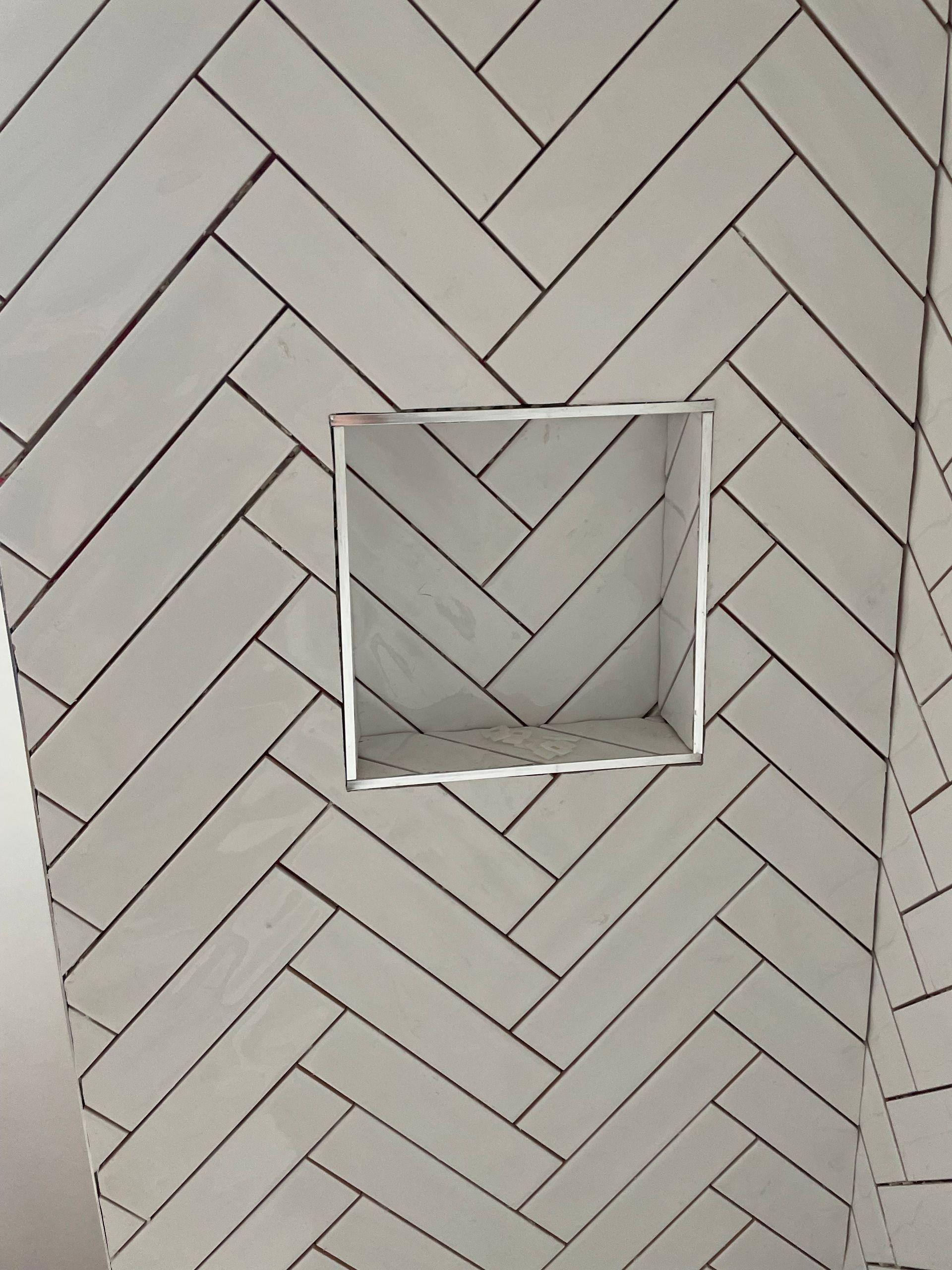 White herringbone-tile wall with a square recessed opening in the center